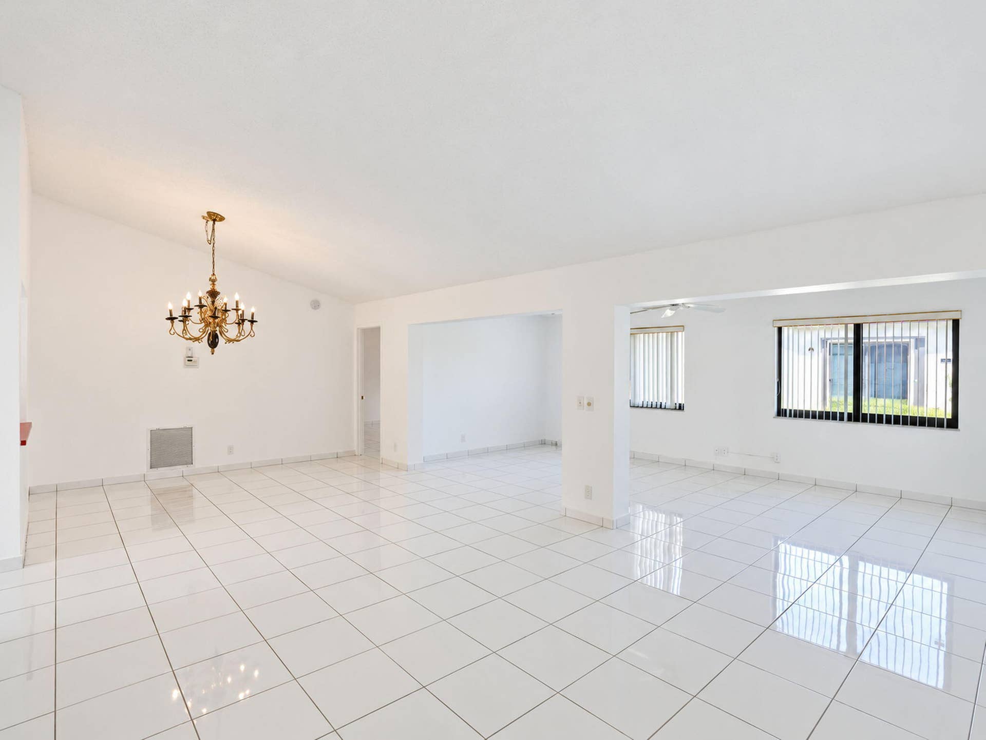2079 SW 16TH Circle, Deerfield Beach, FL 33442 Open-concept interior featuring vaulted ceilings, polished tile flooring, a multi-arm metallic chandelier, and horizontal window blinds