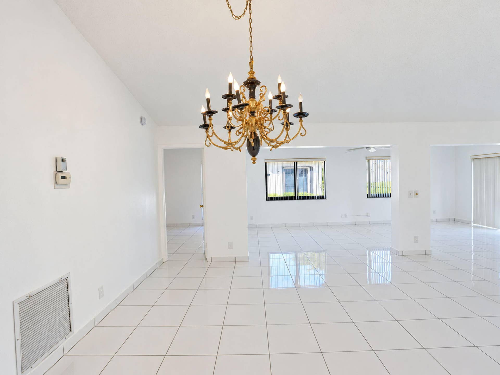 2079 SW 16TH Circle, Deerfield Beach, FL 33442 Open interior space featuring vaulted ceilings, polished ceramic tile flooring, a multi-tiered gold-tone chandelier, and large windows with horizontal blinds
