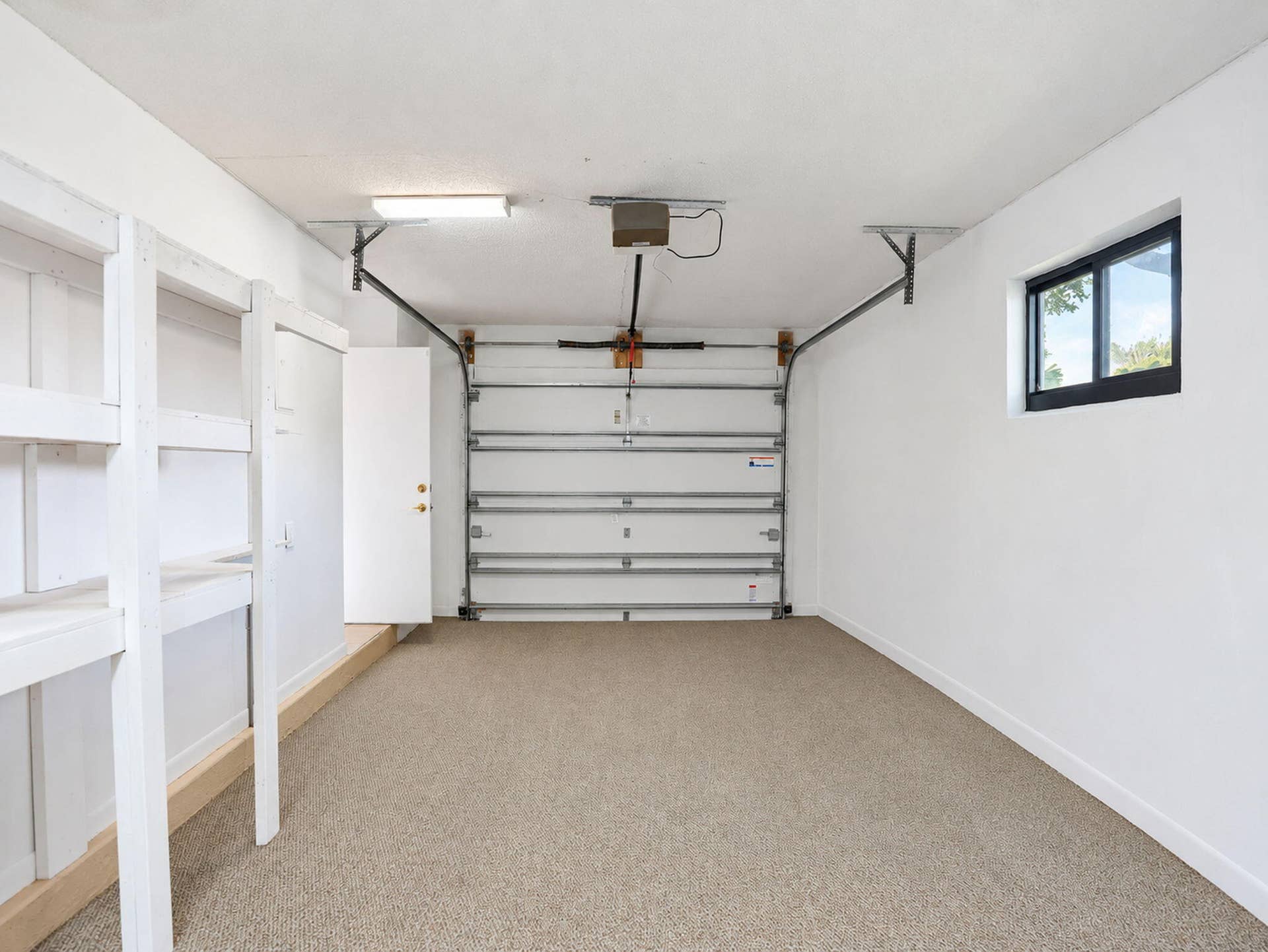 2079 SW 16TH Circle, Deerfield Beach, FL 33442 Finished garage featuring white walls, textured flooring, built-in shelving, an automatic overhead door, and a single-pane window