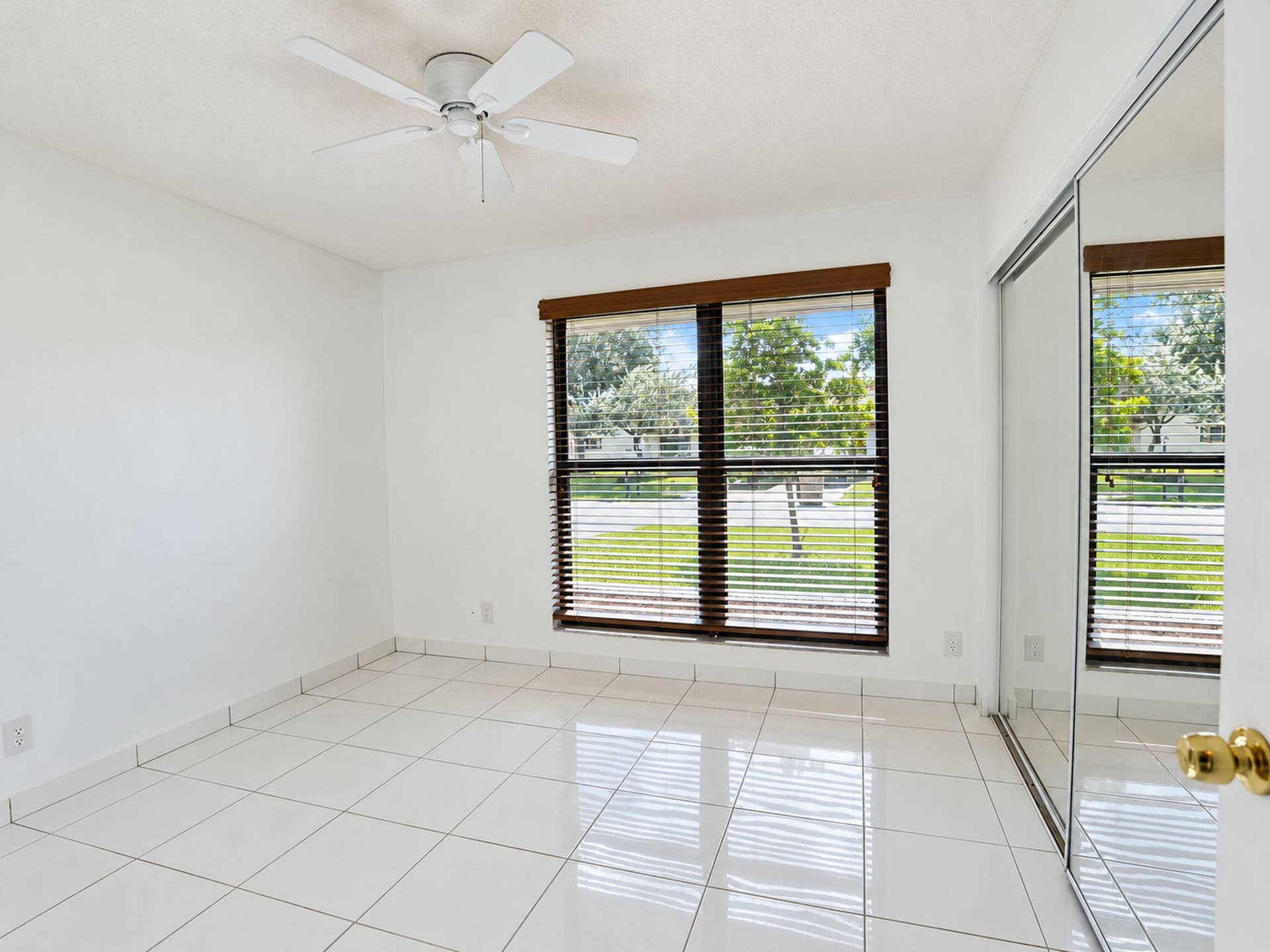 2079 SW 16TH Circle, Deerfield Beach, FL 33442 Neutral tile flooring, ceiling fan, double-hung window with dark wood-finish blinds, and floor-to-ceiling mirrored closet doors