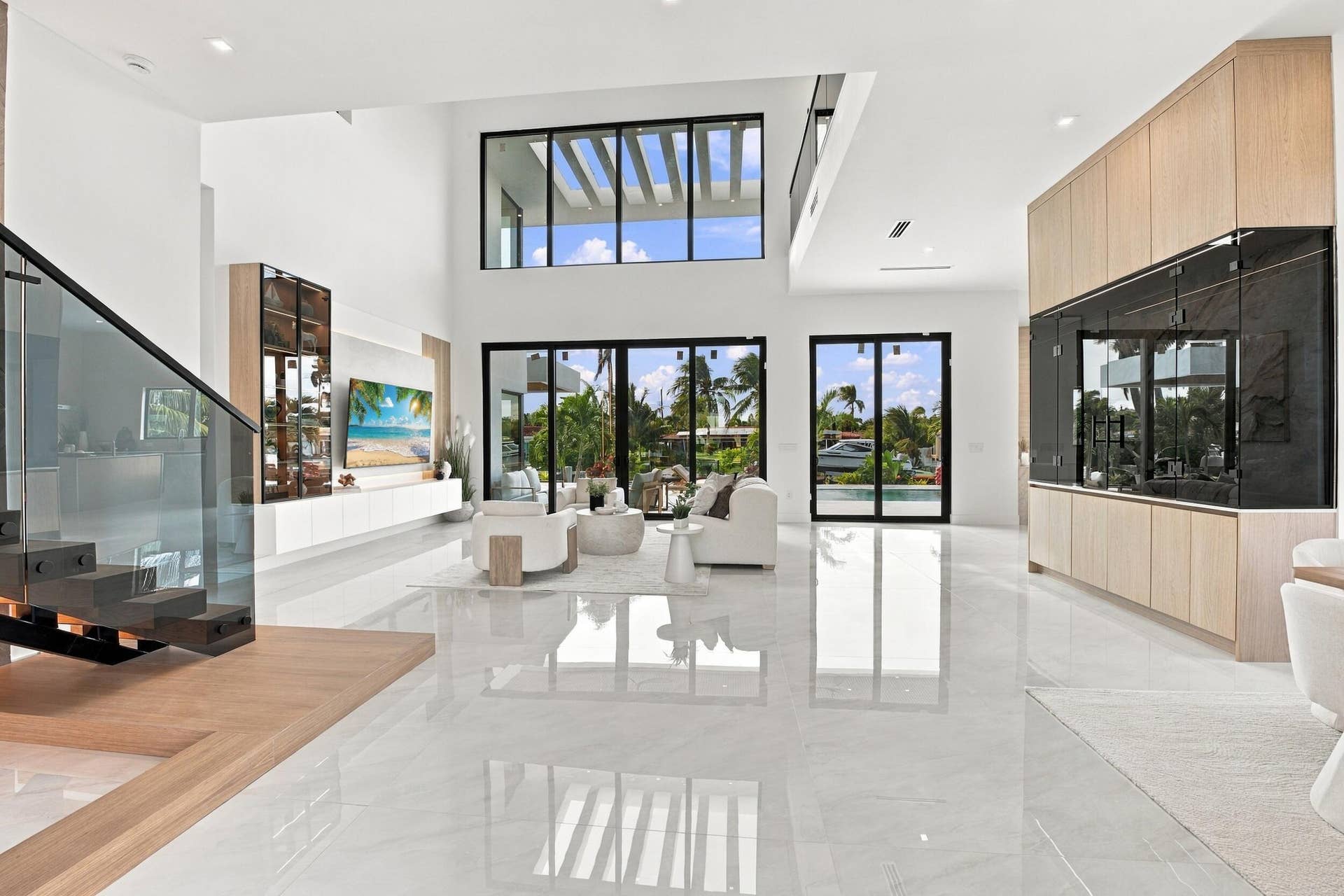 4931 NE 25TH Avenue, Lighthouse Point, FL 33064 Double-height living area featuring floor-to-ceiling glass doors, large-format tile flooring, a custom staircase with glass railing, and built-in floor-to-ceiling cabinetry