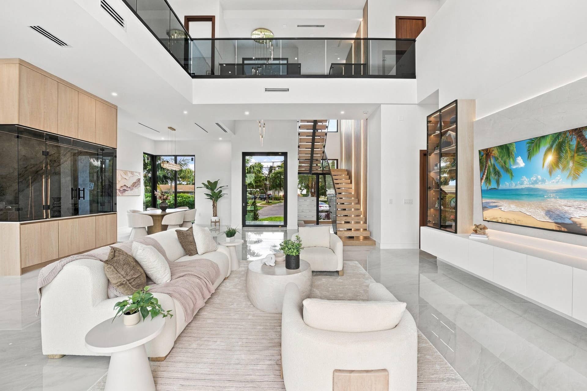 4931 NE 25TH Avenue, Lighthouse Point, FL 33064 Double-height living area featuring floor-to-ceiling cabinetry, a floating staircase with glass balustrades, large-format tile flooring, and integrated media wall cabinetry