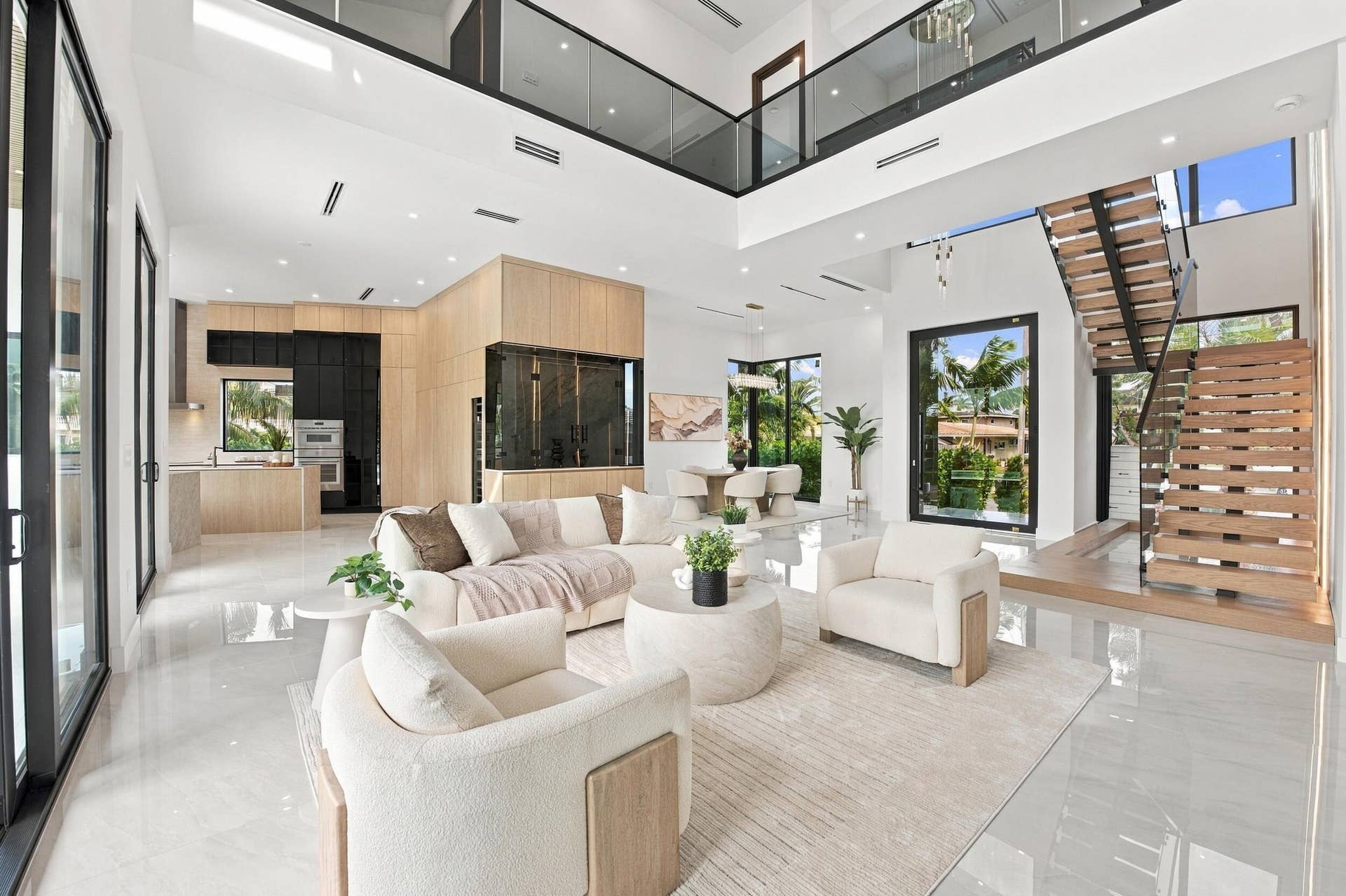 4931 NE 25TH Avenue, Lighthouse Point, FL 33064 Open-concept interior featuring double-height ceilings, a wood-tread staircase with glass railing, large-format polished tile flooring, floor-to-ceiling cabinetry, and expansive glass doors