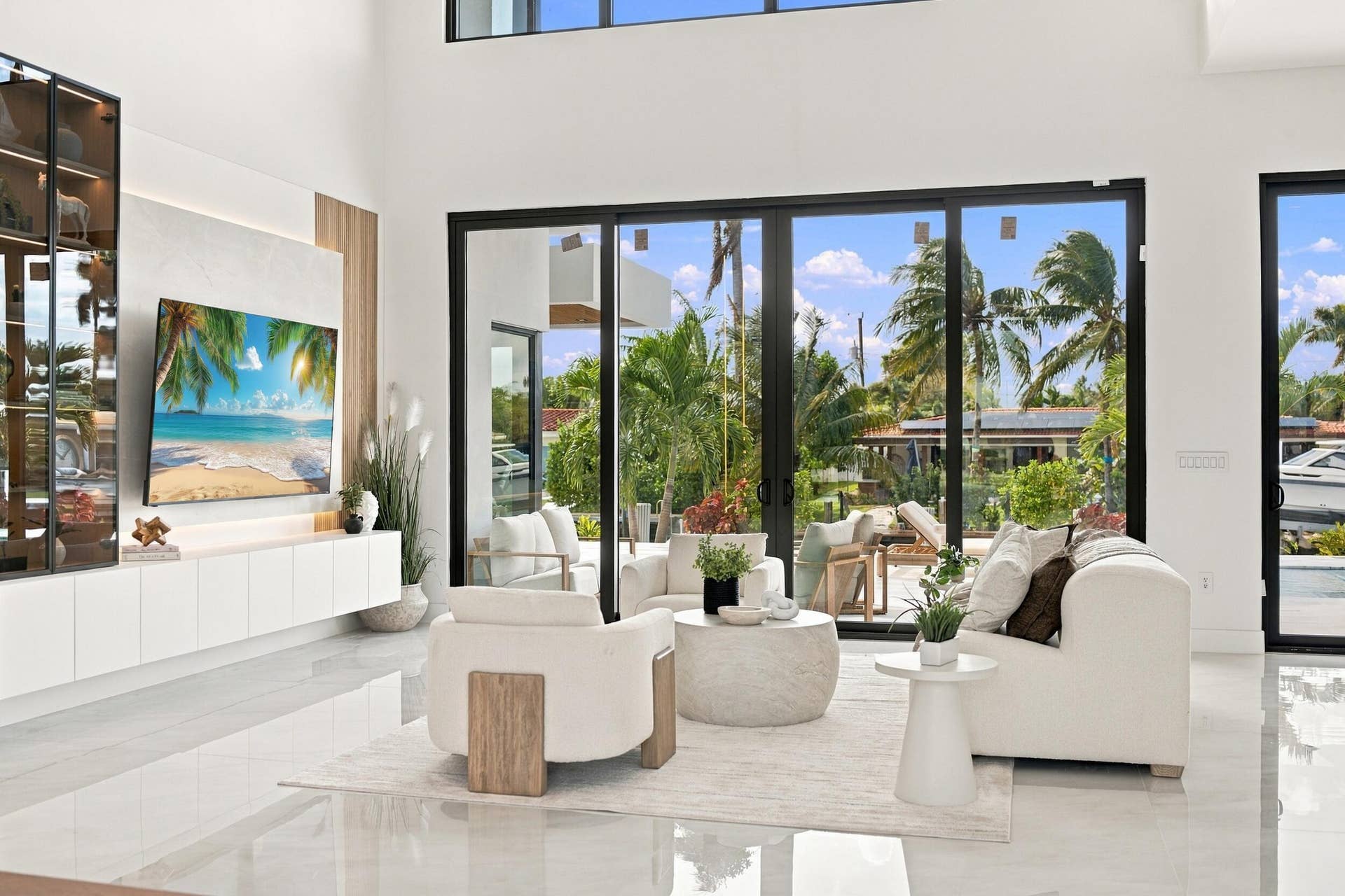 4931 NE 25TH Avenue, Lighthouse Point, FL 33064 Double-height living area featuring floor-to-ceiling glass sliding doors, stone-finish flooring, and built-in minimalist cabinetry with recessed lighting