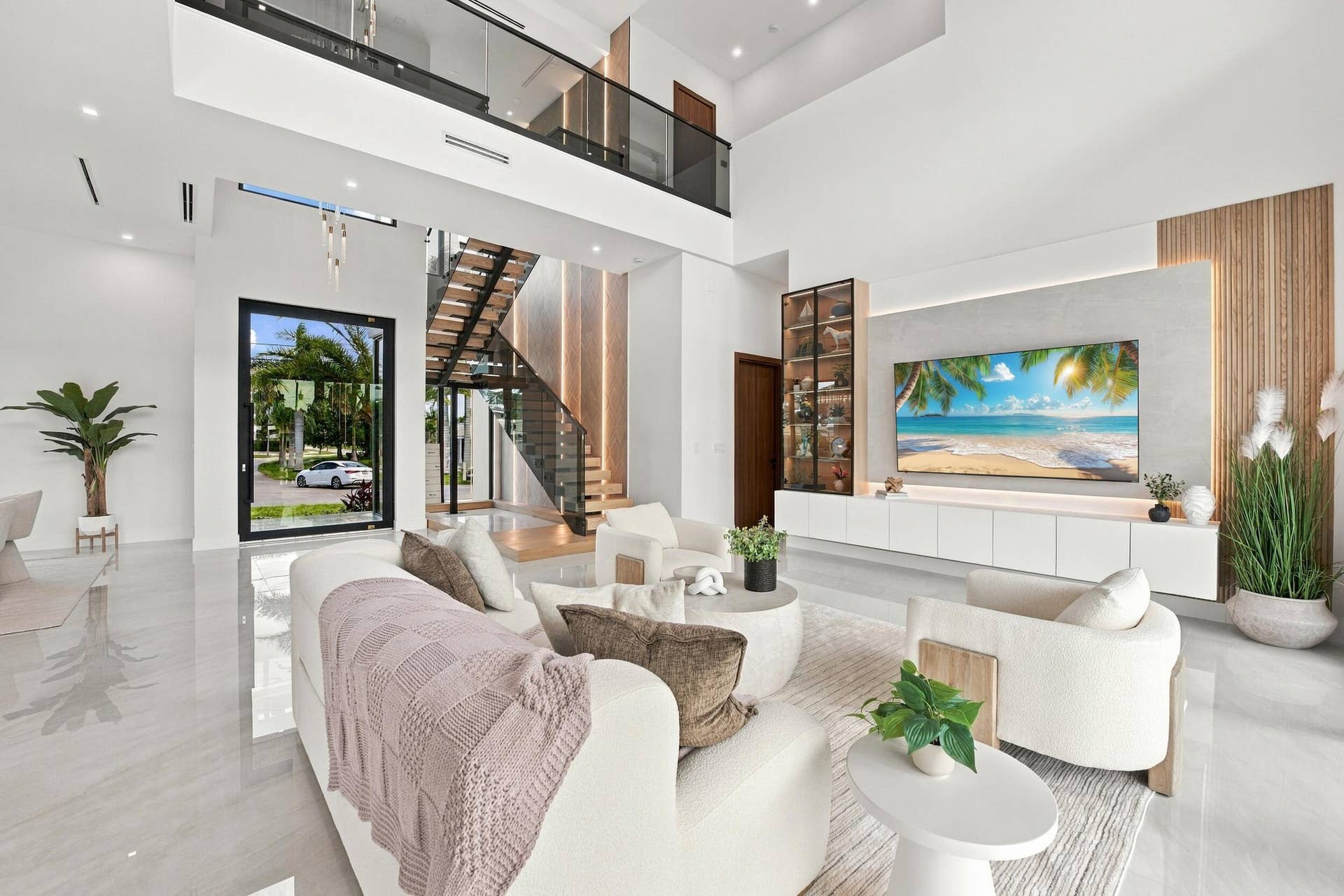 4931 NE 25TH Avenue, Lighthouse Point, FL 33064 Double-height living area featuring floor-to-ceiling windows, porcelain flooring, a floating media console with integrated shelving, and an open-riser staircase with a glass railing