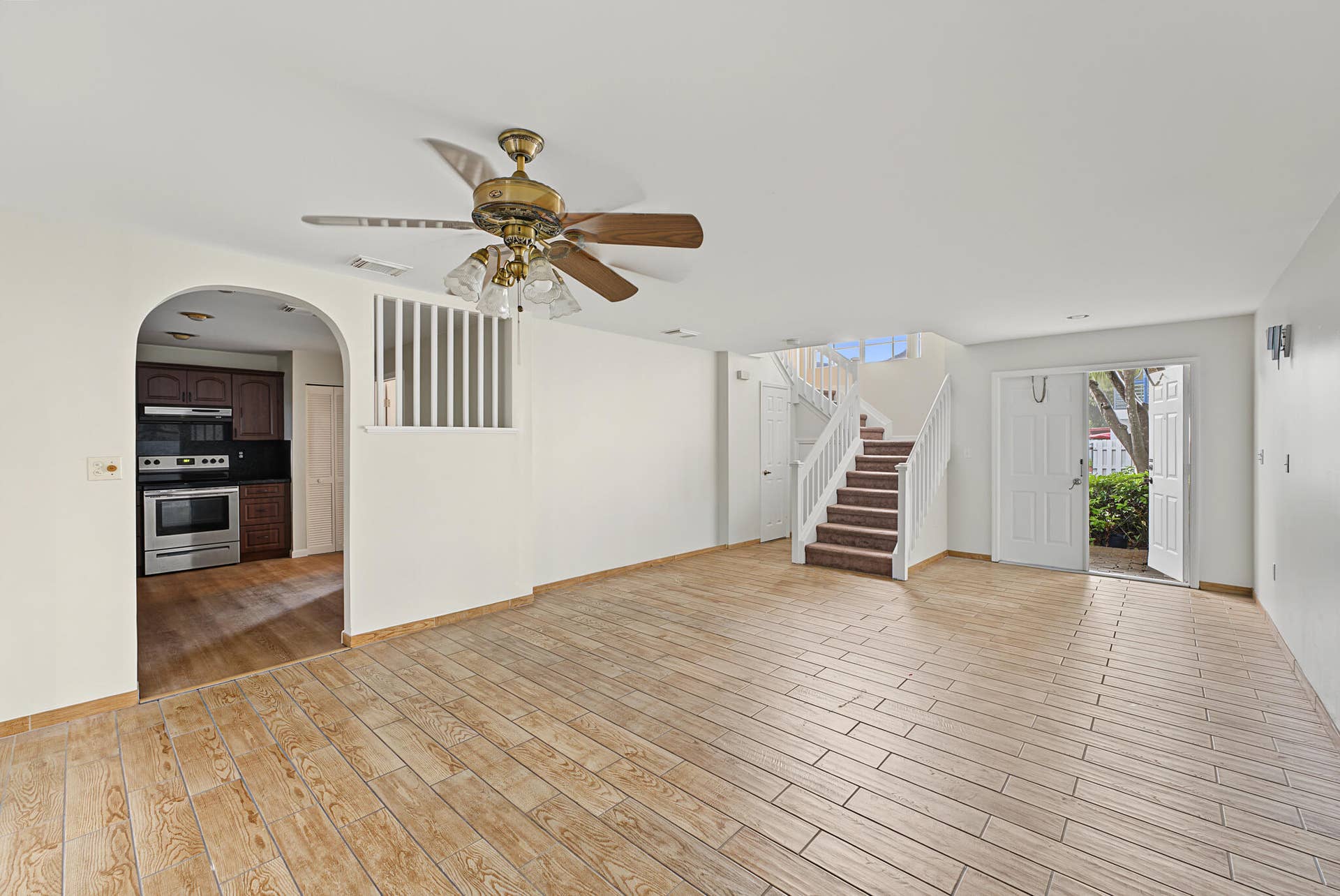 21109 NE 3RD Court, Miami, FL 33179 Open-concept interior featuring wood-finish tile flooring, a centered arched entryway, a built-in ceiling fan with integrated lighting, and a staircase with white balusters