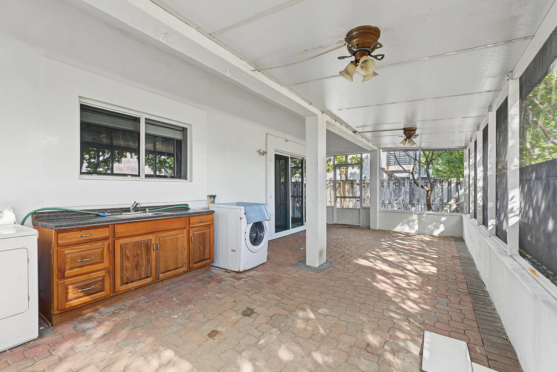 21109 NE 3RD Court, Miami, FL 33179 Covered screened-in patio featuring brick paver flooring, built-in wooden cabinetry with a sink, dual ceiling fans, and sliding glass entry doors