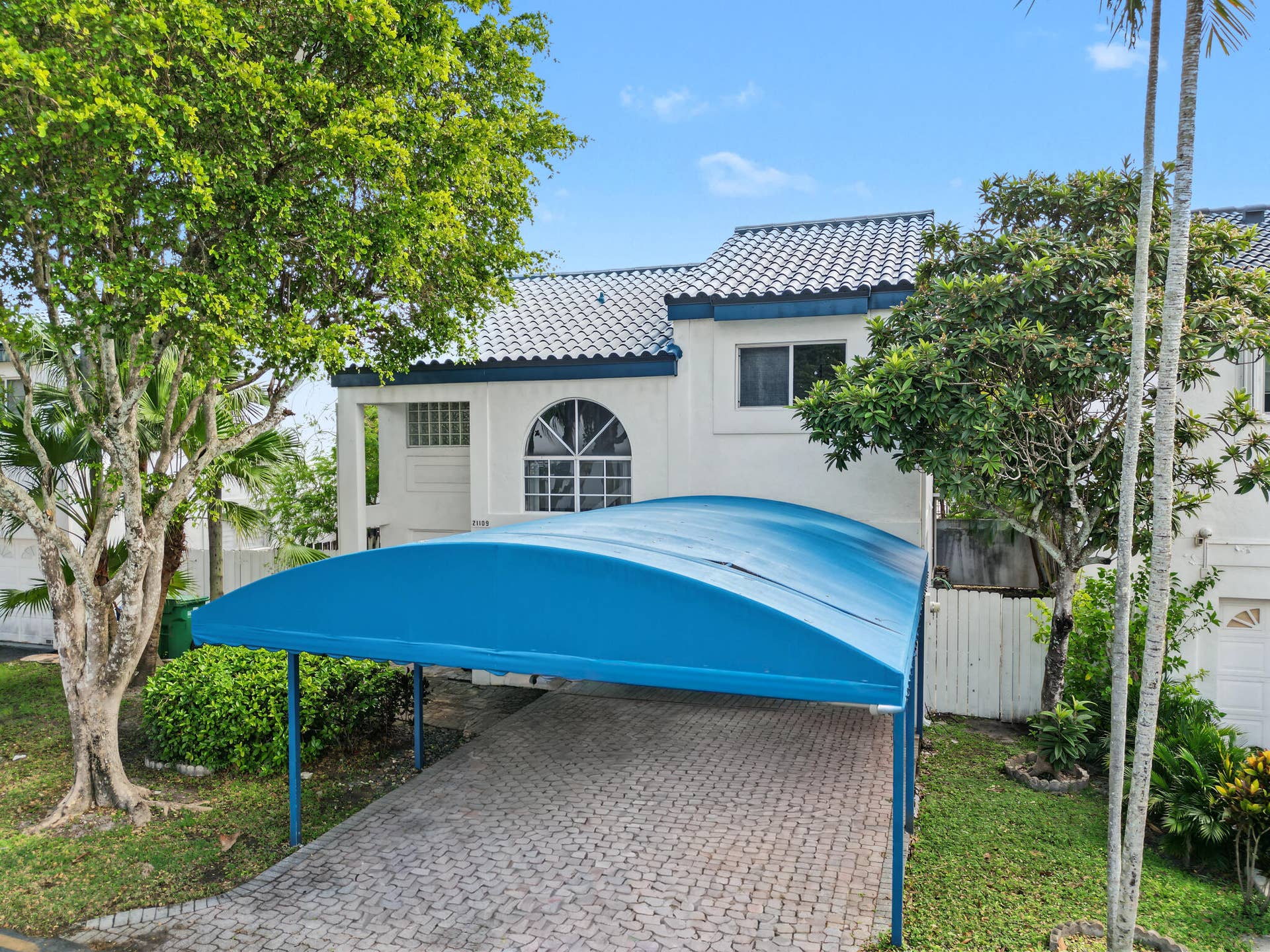 21109 NE 3RD Court, Miami, FL 33179 Stucco exterior featuring a tiled roof, arched window, and paved driveway with a covered carport