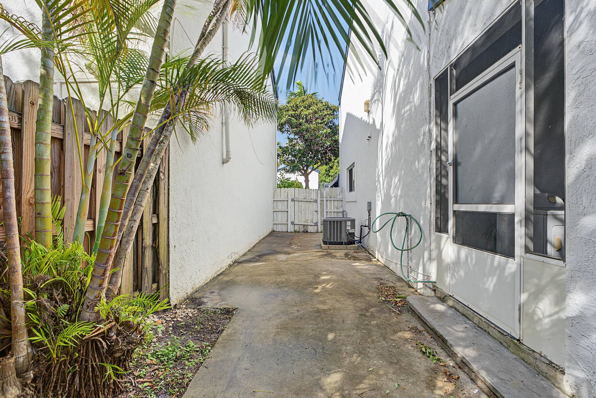 21109 NE 3RD Court, Miami, FL 33179 Exterior side yard featuring a concrete pathway, white wood-slat privacy fencing, stucco exterior walls, and a screened entry door