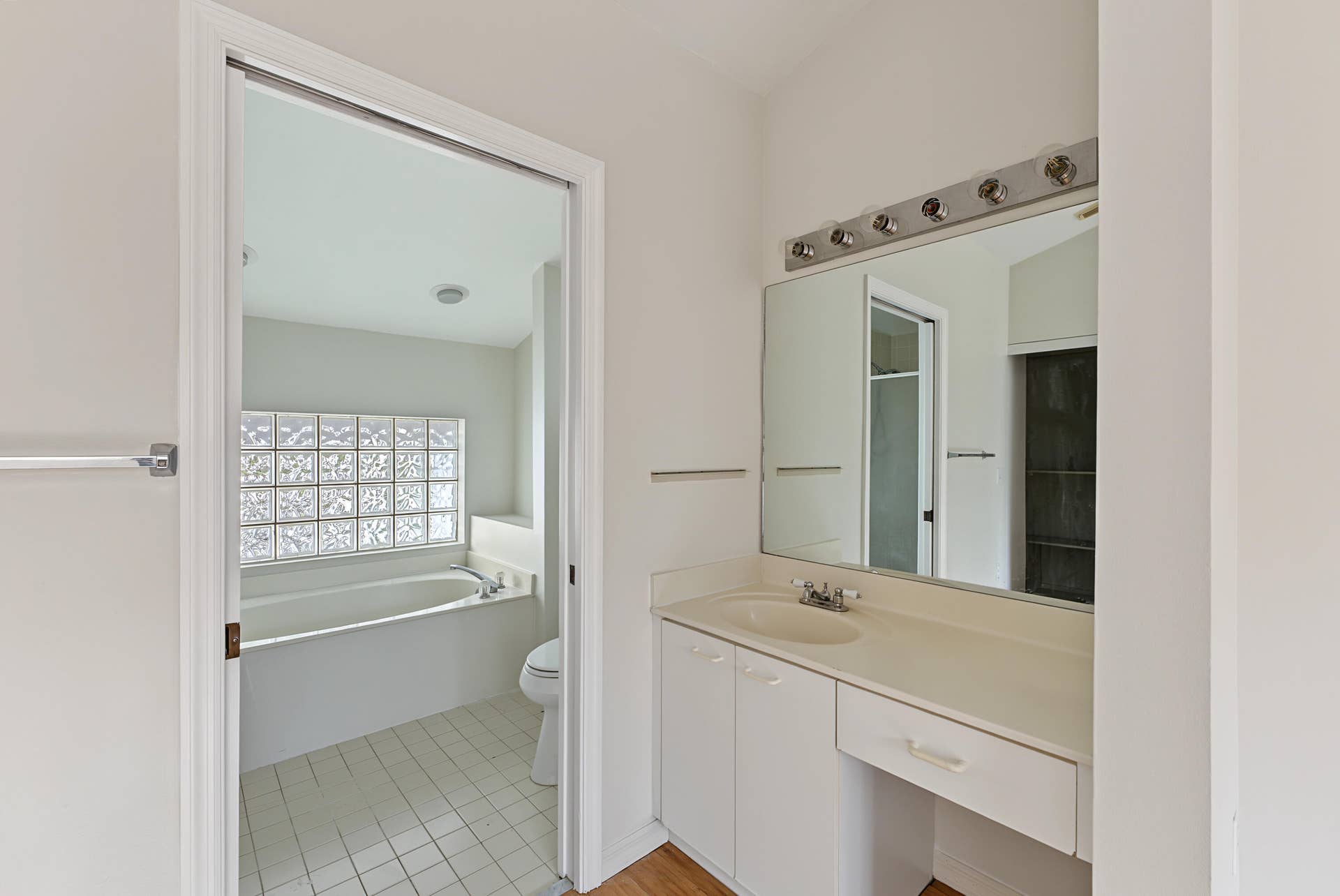 21109 NE 3RD Court, Miami, FL 33179 Bathroom featuring white cabinetry, integrated countertop with oval sink, large rectangular mirror, and multi-bulb vanity light, with a secondary space containing a built-in soaking tub and glass block window