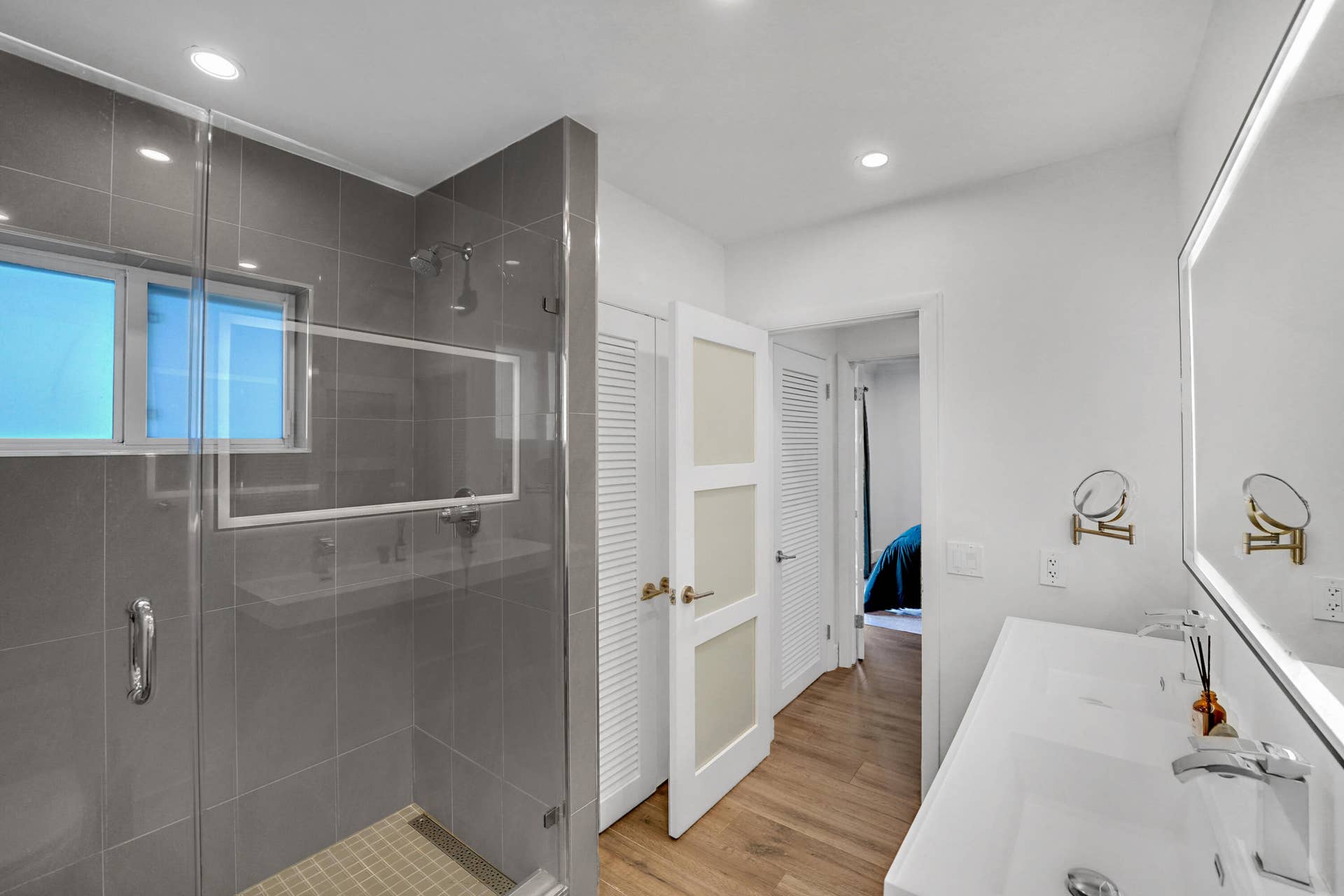 380 NW 35TH Court, Oakland Park, FL 33309 Walk-in shower with grey tile surround, dual-sink vanity, backlit vanity mirror, recessed lighting.