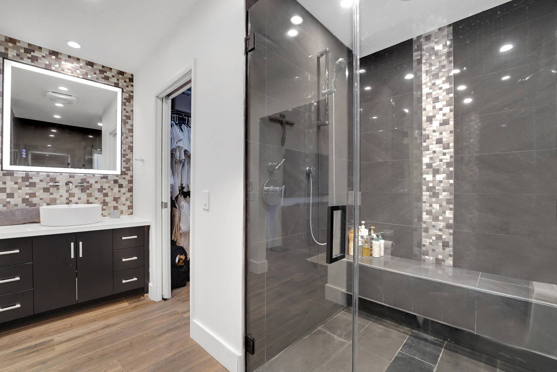 380 NW 35TH Court, Oakland Park, FL 33309 Bathroom featuring a dark wood-finish vanity with a vessel sink, a backlit mirror, wood-finish flooring, and a glass-enclosed walk-in shower with tile detailing and a built-in bench