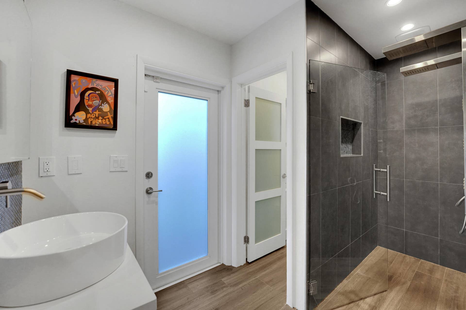380 NW 35TH Court, Oakland Park, FL 33309 Bathroom featuring a vessel sink with a wall-mounted faucet, a glass-enclosed walk-in shower with dark tile surround and integrated niche, and frosted-glass panel doors