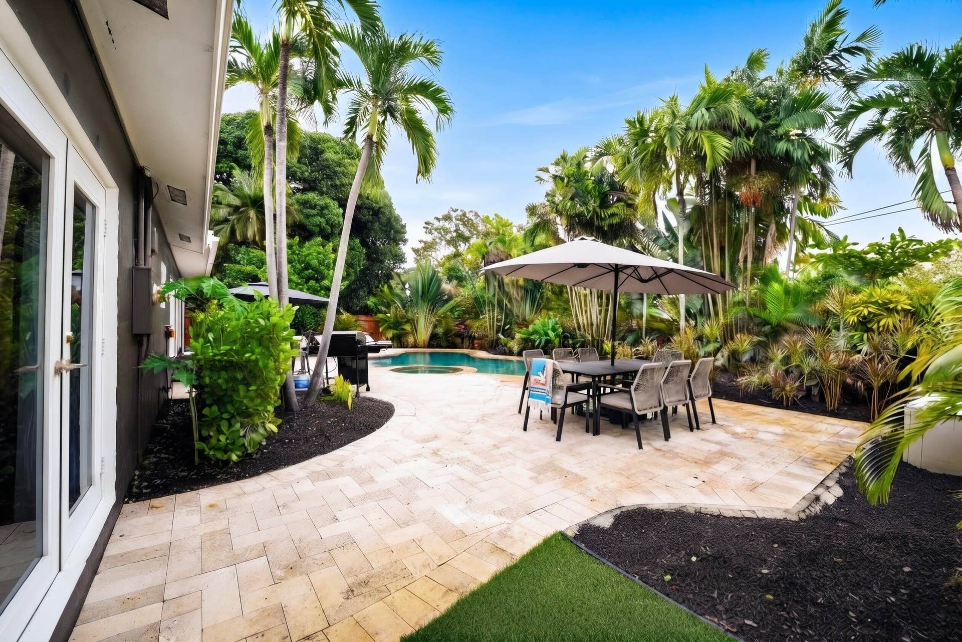 380 NW 35TH Court, Oakland Park, FL 33309 Backyard oasis featuring a paver patio, in-ground swimming pool with an attached spa, lush tropical landscaping, and mature palm trees