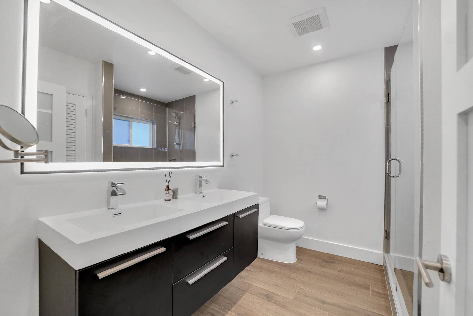 380 NW 35TH Court, Oakland Park, FL 33309 Bathroom featuring a dual-sink vanity with dark cabinetry and a stone countertop, a large integrated LED-lit mirror.