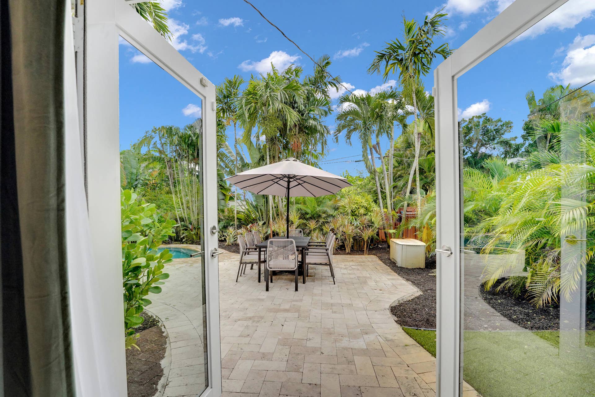 380 NW 35TH Court, Oakland Park, FL 33309 Paver patio featuring a built-in swimming pool, surrounding lush landscaping, and white-framed French door entry