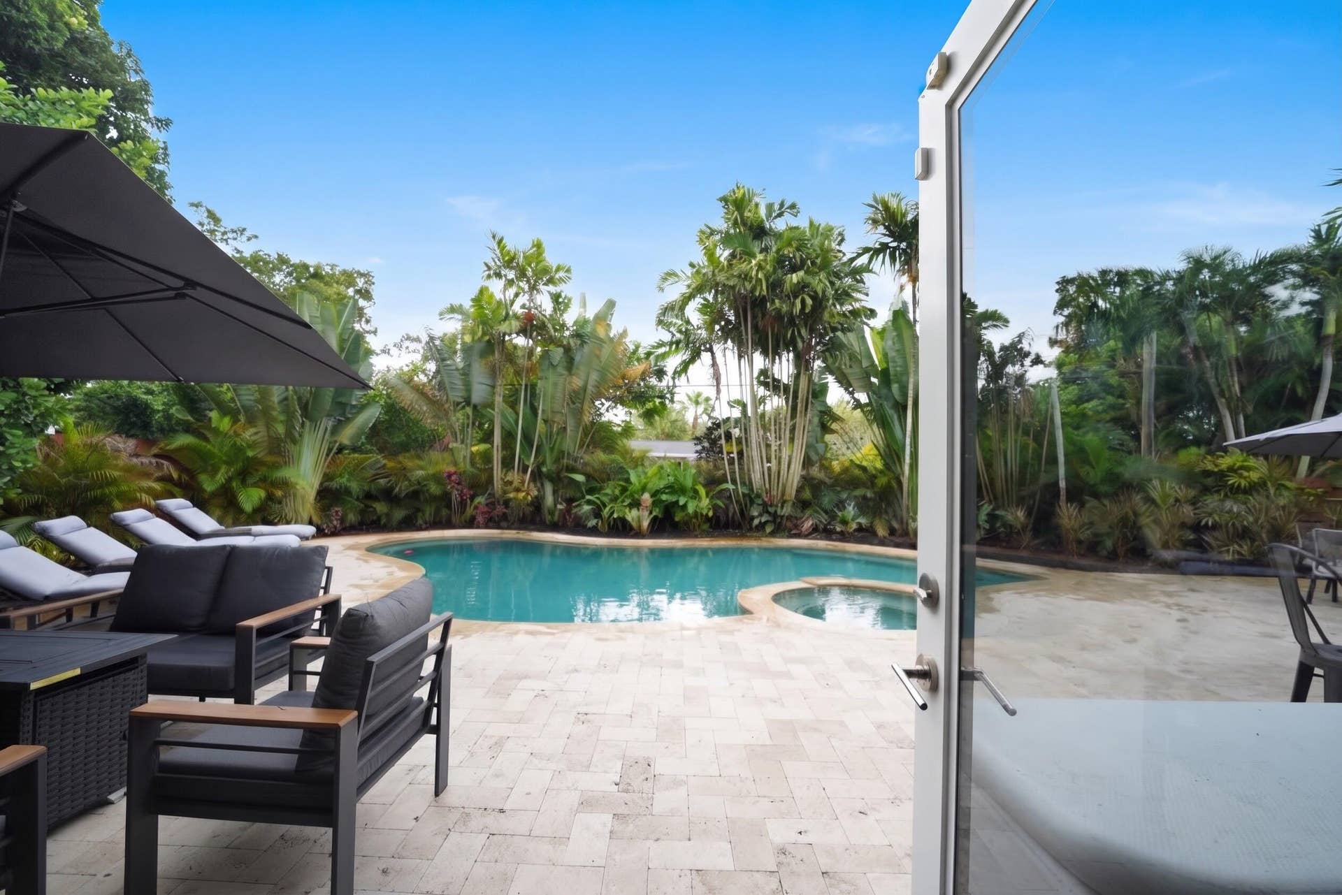380 NW 35TH Court, Oakland Park, FL 33309 Backyard area featuring a swimming pool with integrated spa, paved stone decking, and mature tropical landscaping