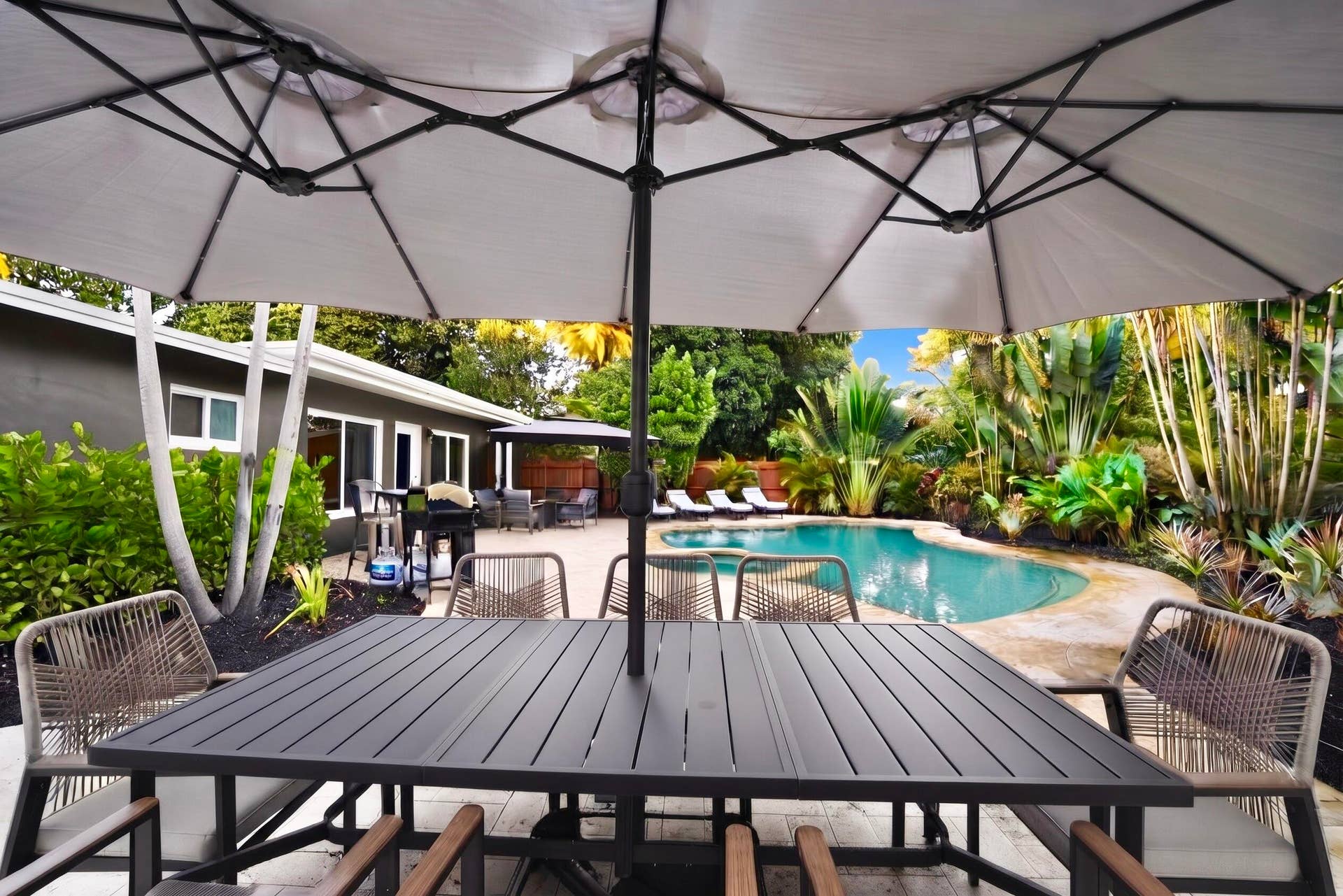 380 NW 35TH Court, Oakland Park, FL 33309 Outdoor patio featuring stone-paver hardscaping, a swimming pool with an attached spa, and mature tropical landscaping