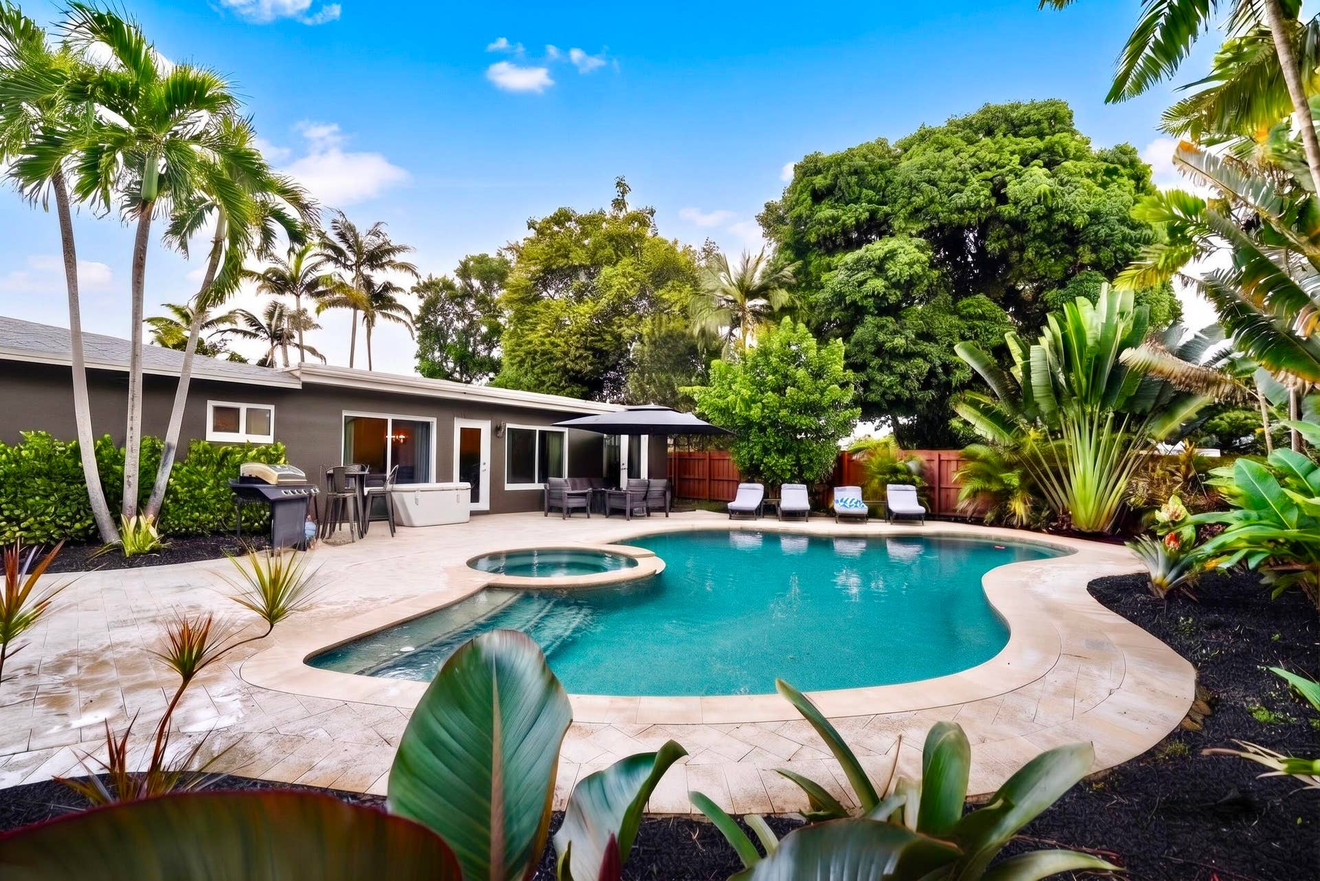 380 NW 35TH Court, Oakland Park, FL 33309 Backyard oasis featuring an in-ground pool with an integrated spa, stone-paver patio, mature palms, and tropical landscaping