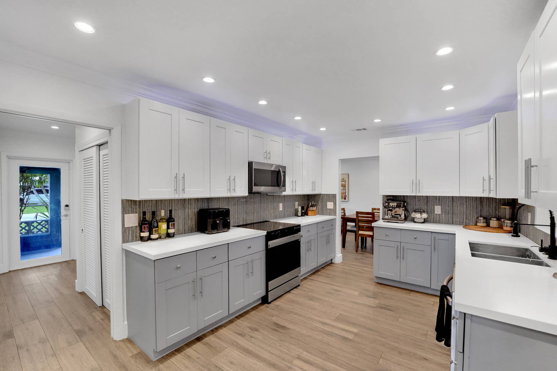 380 NW 35TH Court, Oakland Park, FL 33309 Kitchen featuring two-tone shaker-style cabinetry, quartz countertops, tile backsplash, recessed lighting, and wood-finish flooring