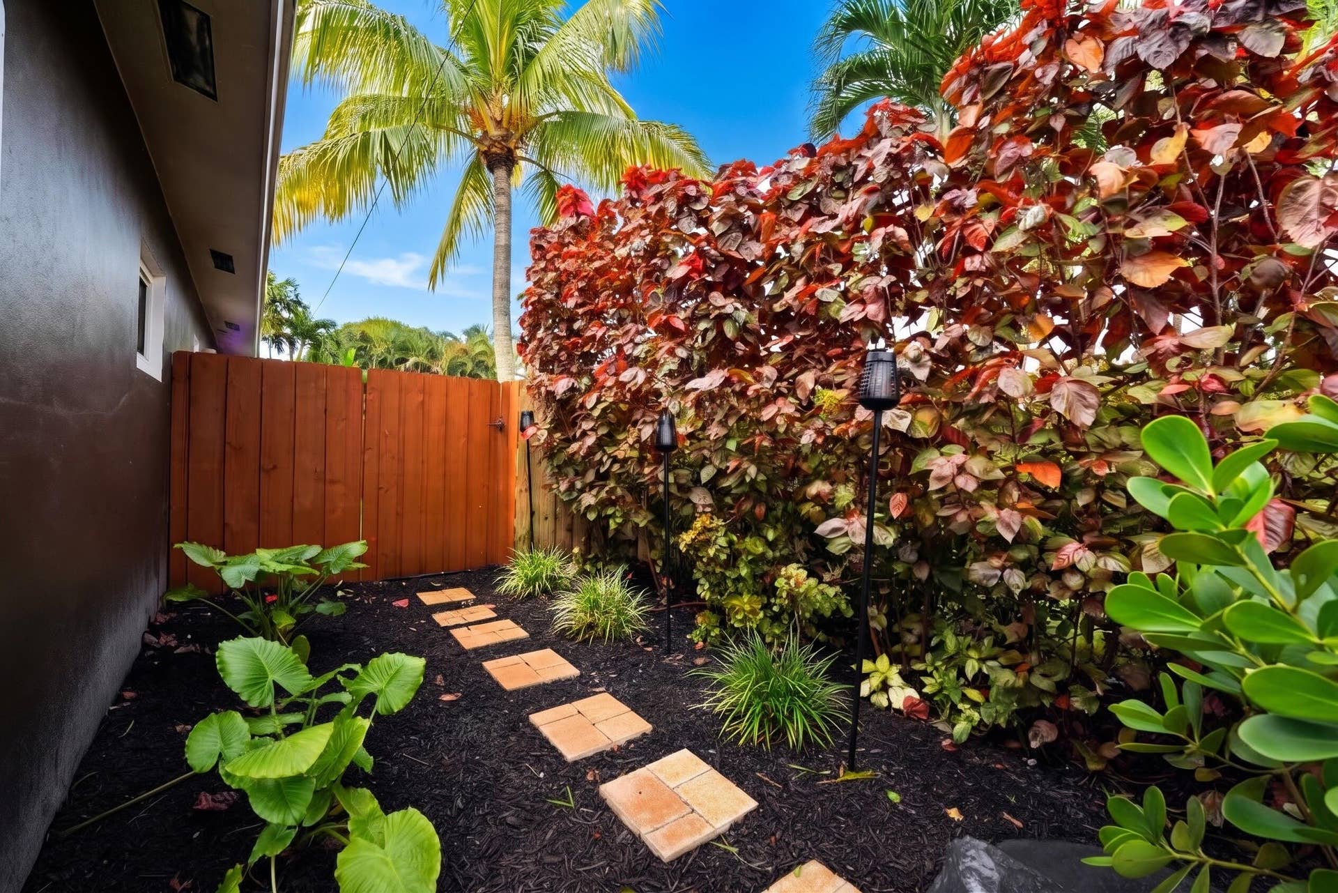 380 NW 35TH Court, Oakland Park, FL 33309 Landscaped side yard featuring a paver stone walkway, dark mulch garden beds, mature tropical plantings, and a wood privacy fence