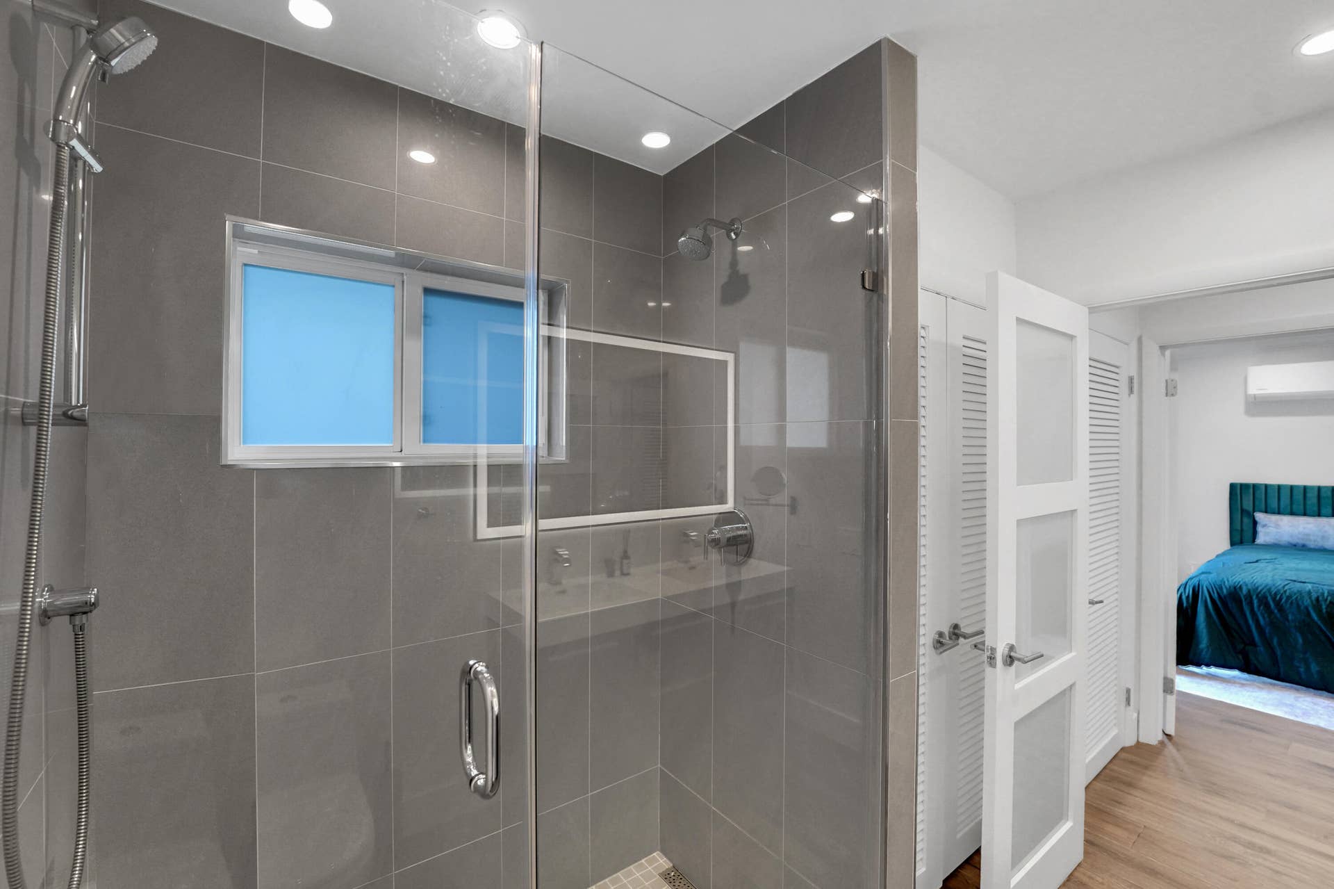 380 NW 35TH Court, Oakland Park, FL 33309 Walk-in shower with floor-to-ceiling gray tile, frameless glass enclosure, and dual shower heads including a handheld wand