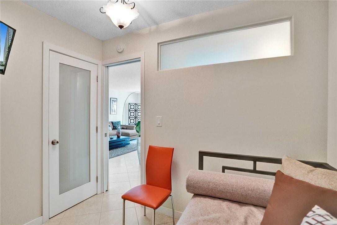 This view of the second bedroom shows the closet and looks out onto the living room. The glass window above the wall allows light into the room. There is a pocket door for privacy.