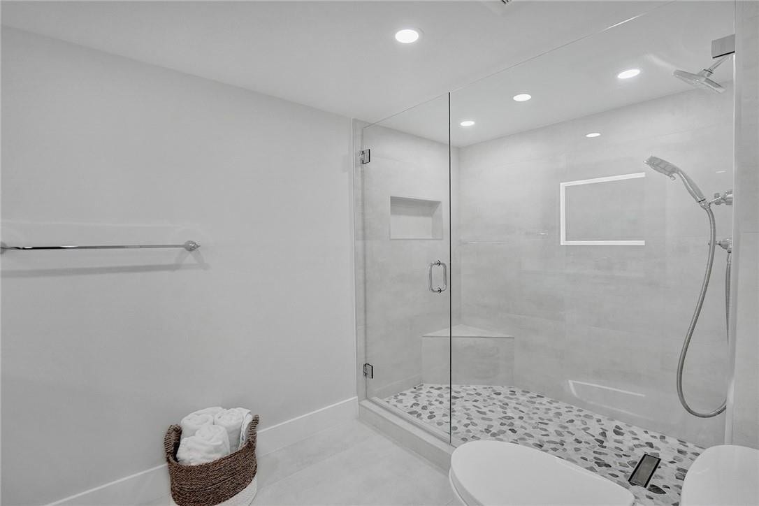 The second bathroom has a frameless glass shower enclosure and stone tile flooring.