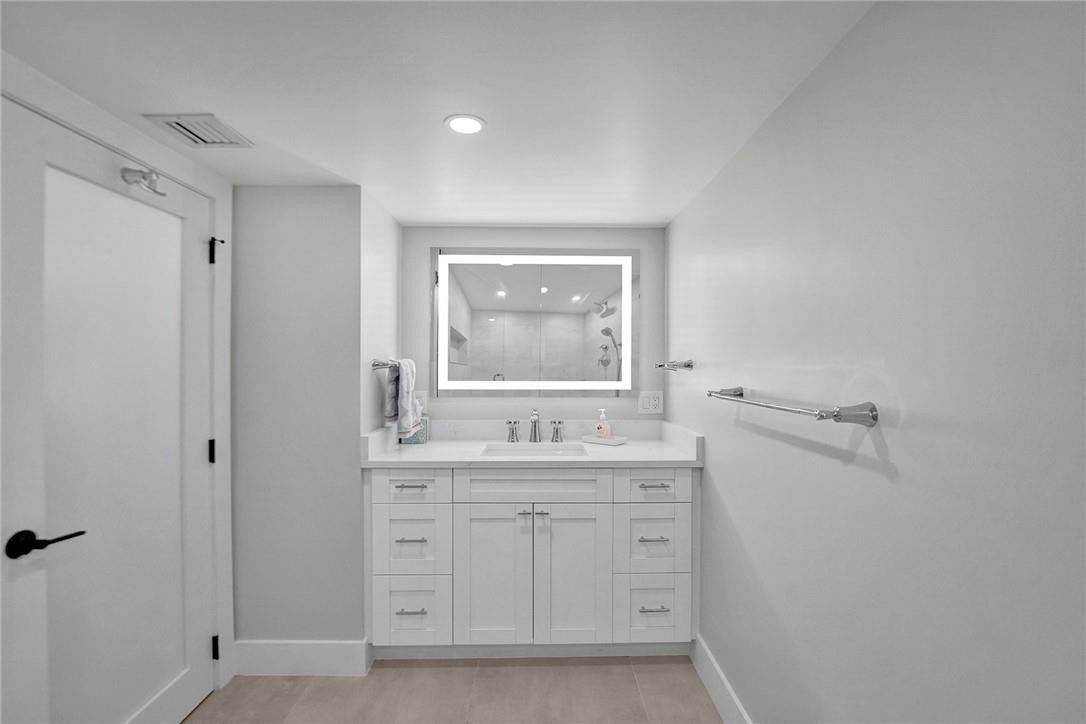 The second bathroom has a recessed lighting, illuminated mirror, a quartz countertop on the vanity, Moen hardware, and a lighter yet still beachy porcelain tile flooring.