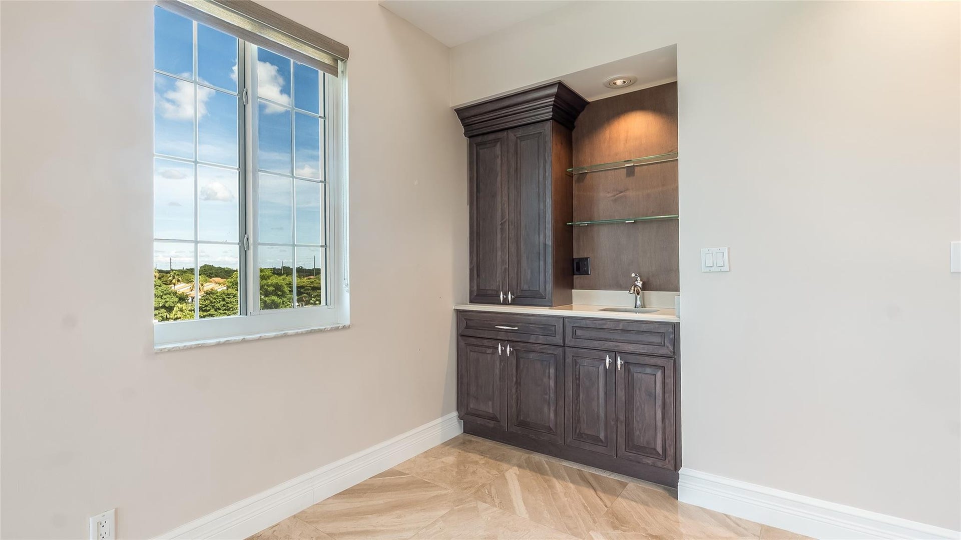 4116 W Palm Aire Drive, #166b, Pompano Beach, FL 33069 Built-in wet bar with glass shelving and dark wood cabinetry, perfectly positioned for seamless entertaining.