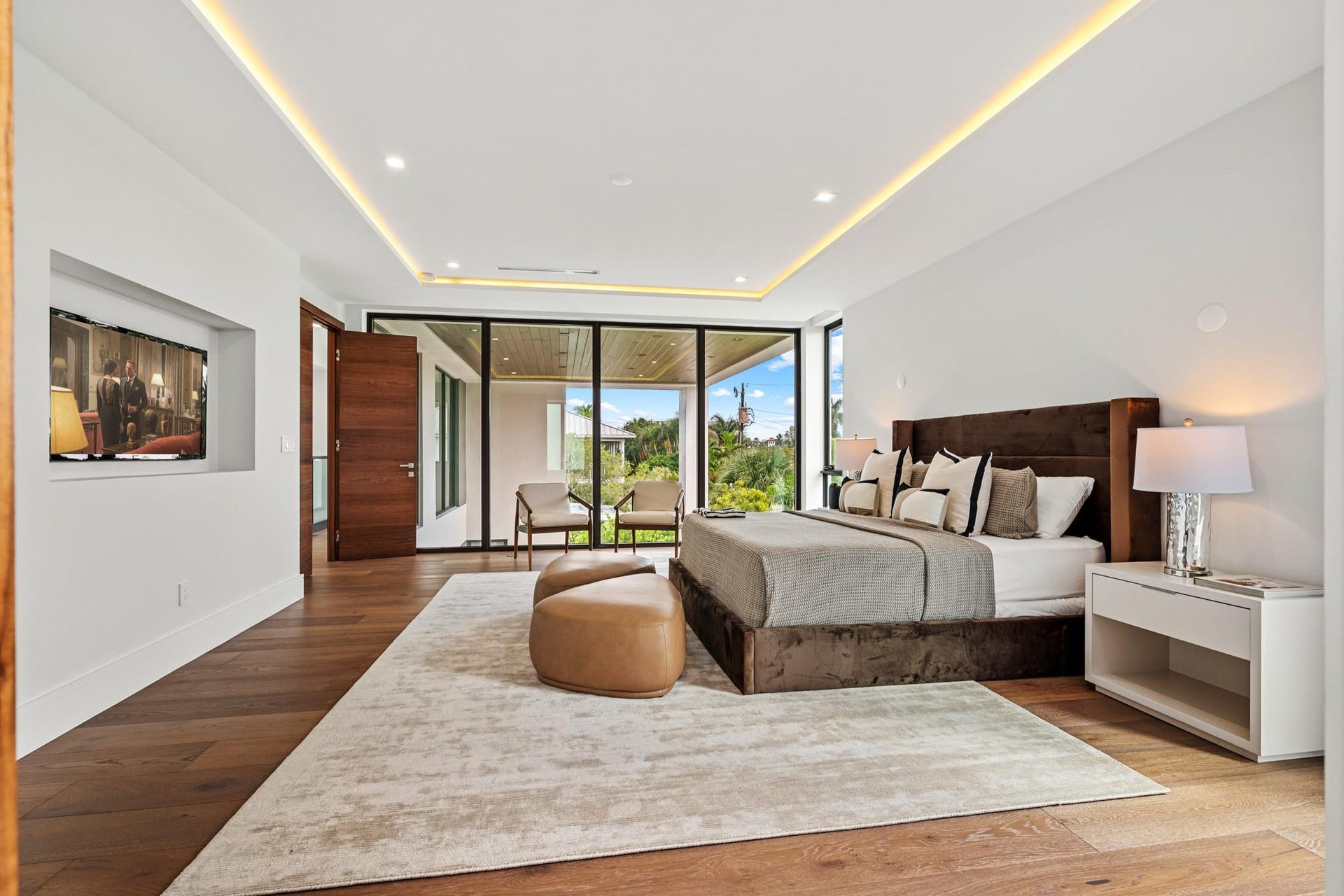 2000 Harbourview Drive, Fort Lauderdale, FL 33316 A luxurious modern bedroom retreat featuring warm wood flooring, a statement upholstered bed, and seamless access to a private terrace beyond. Clean architectural lines and expansive glass create a serene, light-filled sanctuary designed for elevated comfort.