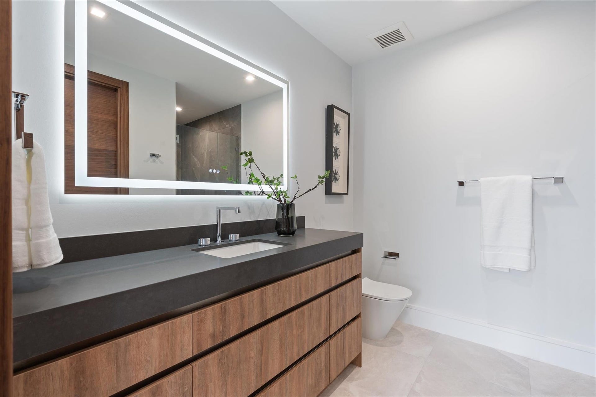 2000 Harbourview Drive, Fort Lauderdale, FL 33316 A sleek, modern bath showcasing a floating wood vanity, expansive mirror, and clean-lined contemporary finishes. Bright and minimalist, this refined space offers spa-like simplicity with warm, natural accents.