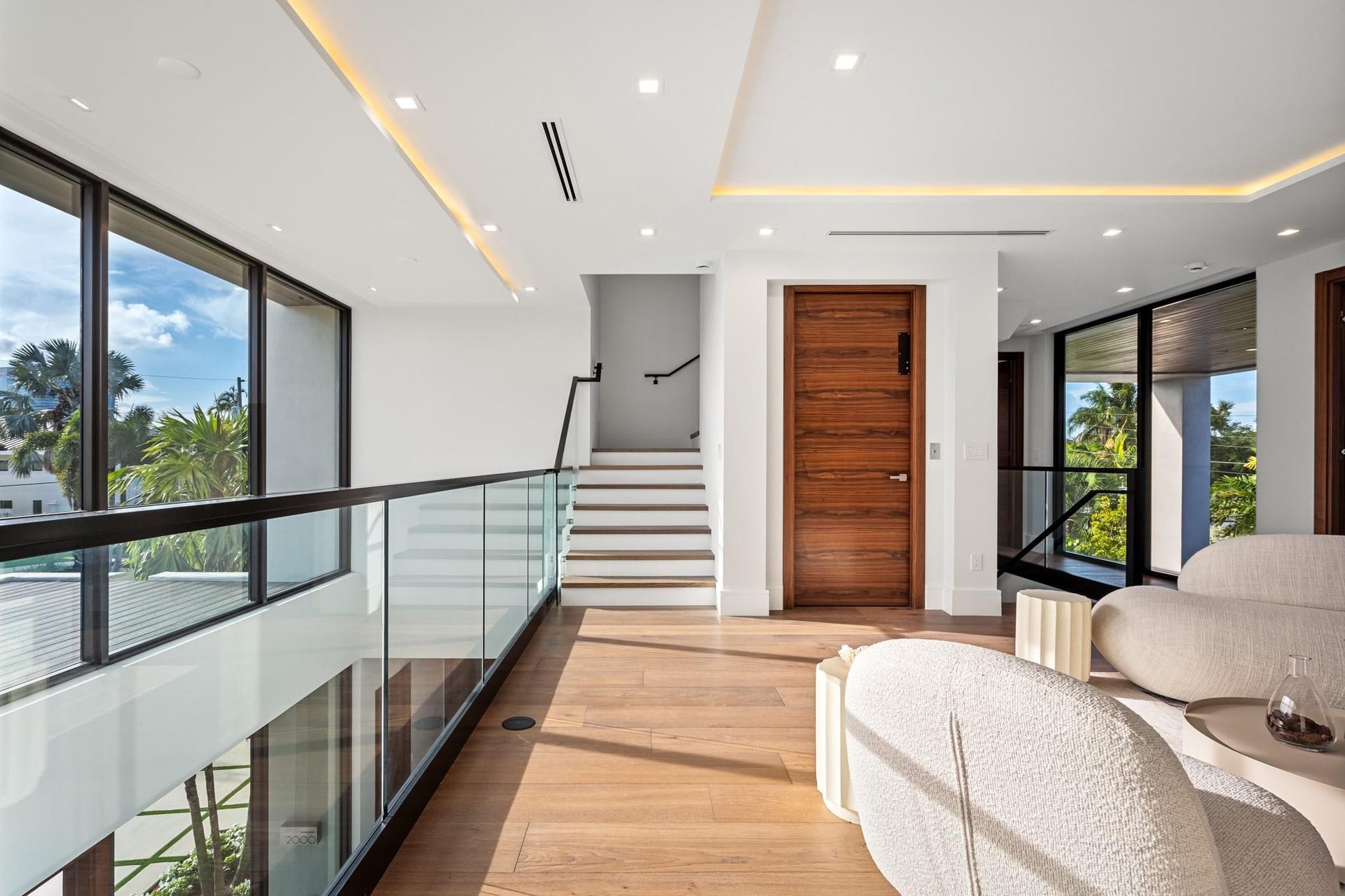 2000 Harbourview Drive, Fort Lauderdale, FL 33316 A striking upper-level gallery hallway featuring warm wood floors, sleek glass railings, and expansive windows that flood the space with natural light. Clean architectural lines and contemporary finishes create a sophisticated transition between the homes private retreats.