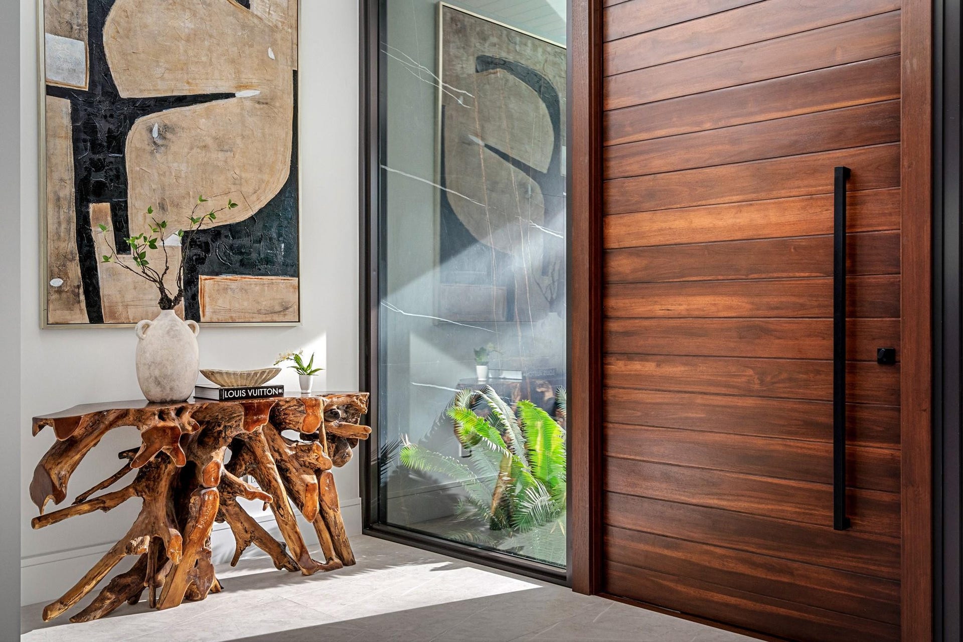 2000 Harbourview Drive, Fort Lauderdale, FL 33316 A sophisticated entry detail featuring a striking wood pivot door, sleek glass panels, and curated contemporary art that creates an immediate design statement. Warm natural textures and clean modern lines set a tone of refined luxury from the moment you arrive.