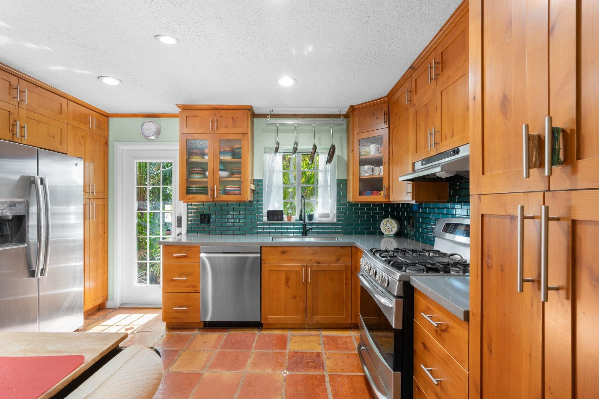 2956 NW 6th Terrace, Wilton Manors, FL 33311 Kitchen with custom wood cabinetry, quartz countertops, and teal subway tile backsplash. Stainless steel appliances and window above the sink provide both function and natural light.