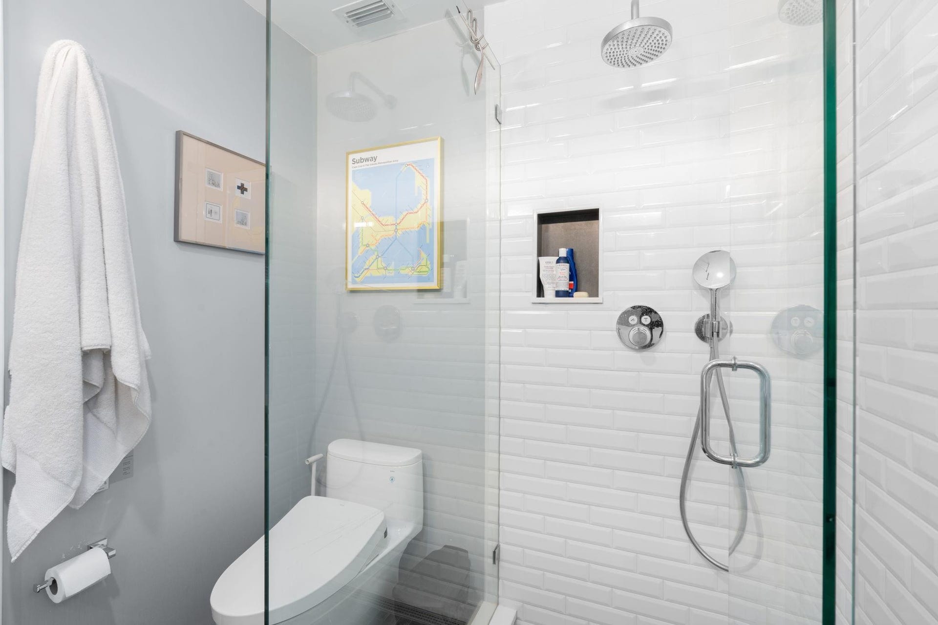 2956 NW 6th Terrace, Wilton Manors, FL 33311 Walk-in shower with glass enclosure, rainfall showerhead, handheld fixture, and recessed niche storage. Light tile surround enhances the bright, streamlined design.