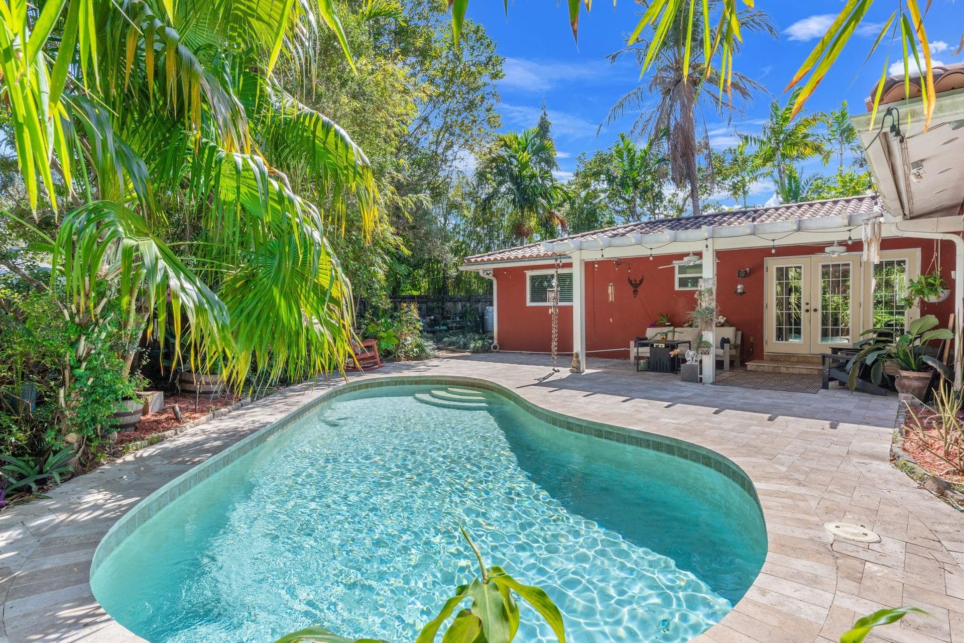 2956 NW 6th Terrace, Wilton Manors, FL 33311 In-ground pool with curved design and step entry, positioned adjacent to the covered patio for easy indoor-outdoor flow. Lush greenery provides natural privacy.