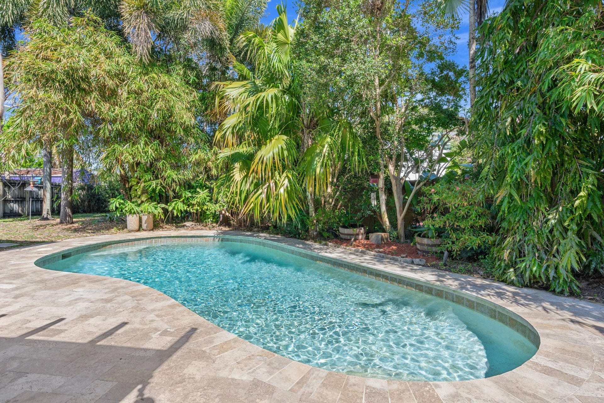2956 NW 6th Terrace, Wilton Manors, FL 33311 Freeform swimming pool surrounded by travertine-style pavers and mature tropical landscaping. Private setting creates a relaxing outdoor retreat.
