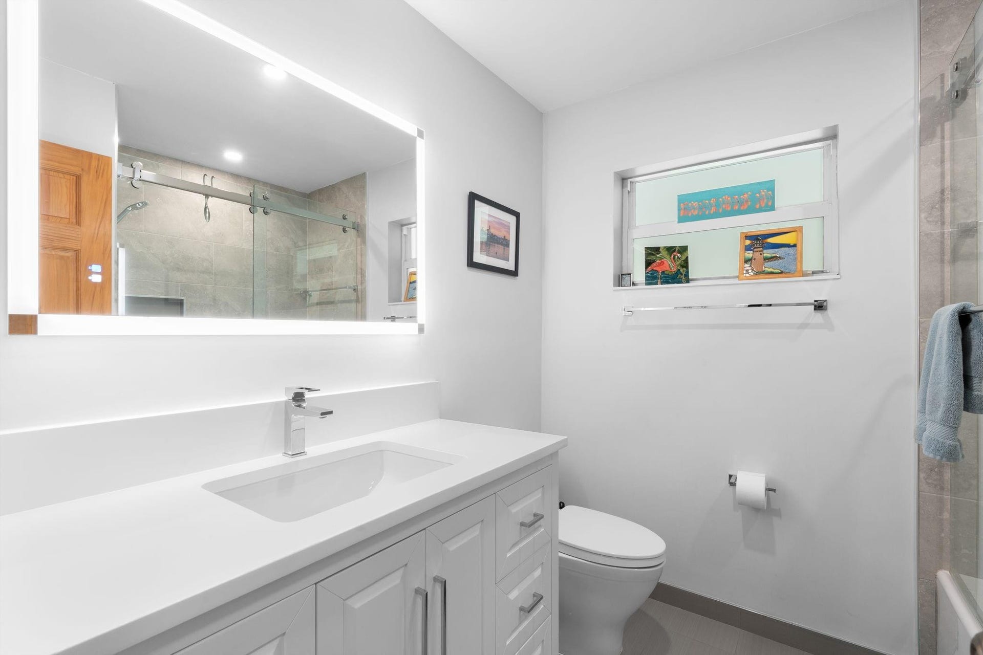 2956 NW 6th Terrace, Wilton Manors, FL 33311 Updated bathroom with single-sink vanity, quartz countertop, and backlit mirror. Frosted window allows natural light while maintaining privacy.