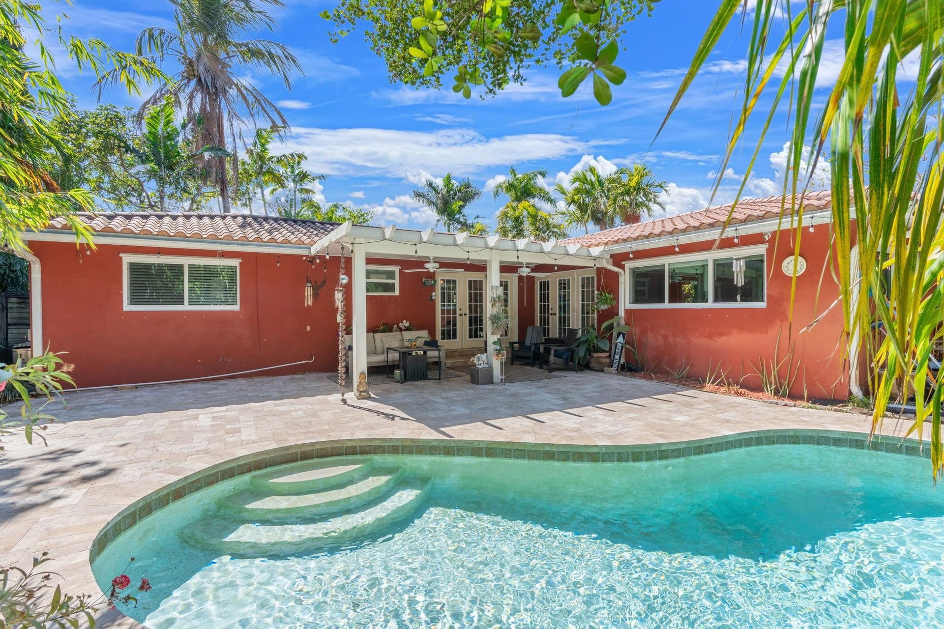 2956 NW 6th Terrace, Wilton Manors, FL 33311 Rear elevation with covered patio, French doors, and multiple windows overlooking the pool. Tile roof and landscaped yard enhance the outdoor setting.