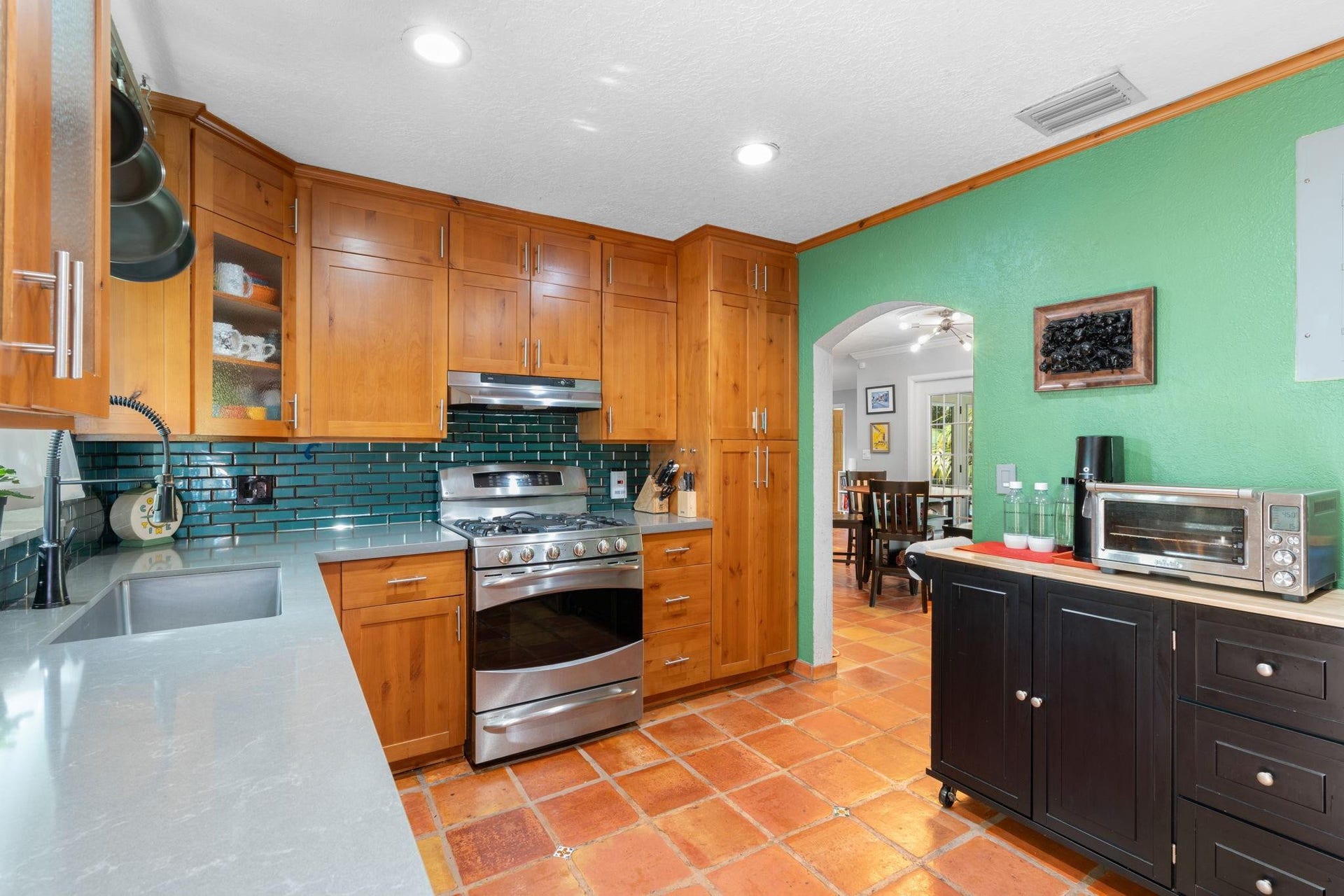 2956 NW 6th Terrace, Wilton Manors, FL 33311 Kitchen featuring custom wood cabinetry, quartz countertops, stainless steel gas range, and glossy subway tile backsplash. Terracotta tile flooring and recessed lighting complete the warm, functional design.
