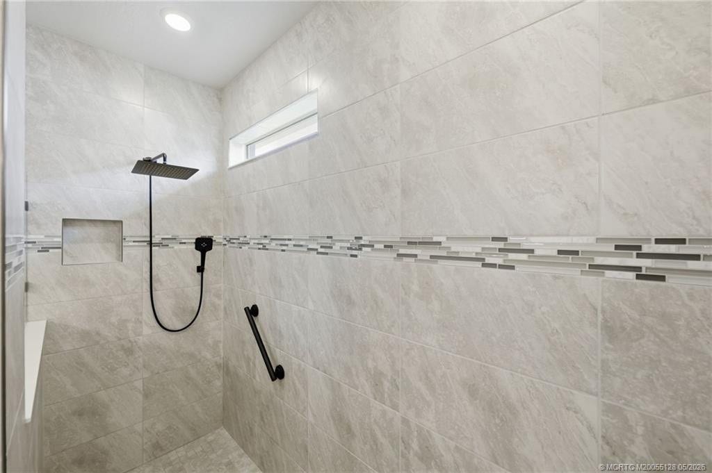 Oversized walk-in primary shower showcases elegant floor-to-ceiling tile, designer accent trim, built-in niche, and upgraded rainfall showerhead. This beautifully finished spa-inspired space offers a luxurious and relaxing retreat with modern style and exceptional attention to detail.