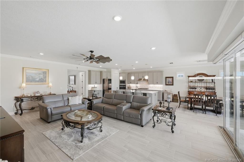Expansive open floor plan offers seamless flow between the living, dining, and kitchen areas, creating the perfect space for entertaining and everyday living. Features include elegant tile flooring, crown molding, recessed lighting, and large sliding glass doors that fill the home with natural light and connect to the outdoor living area and pool.