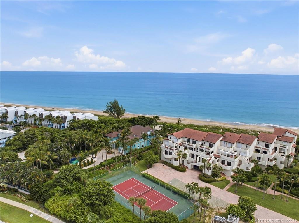Aerial view showcasing the community tennis court surrounded by tropical landscaping, just steps from the beach.