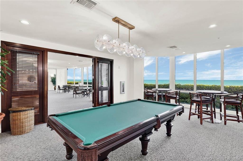 Spacious community billiards room featuring a pool table, comfortable seating, and large windows offering beautiful coastal views.