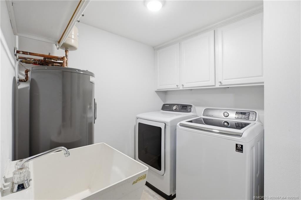 Separate laundry room featuring a full-size washer and dryer, utility sink, and overhead cabinetry for additional storage.