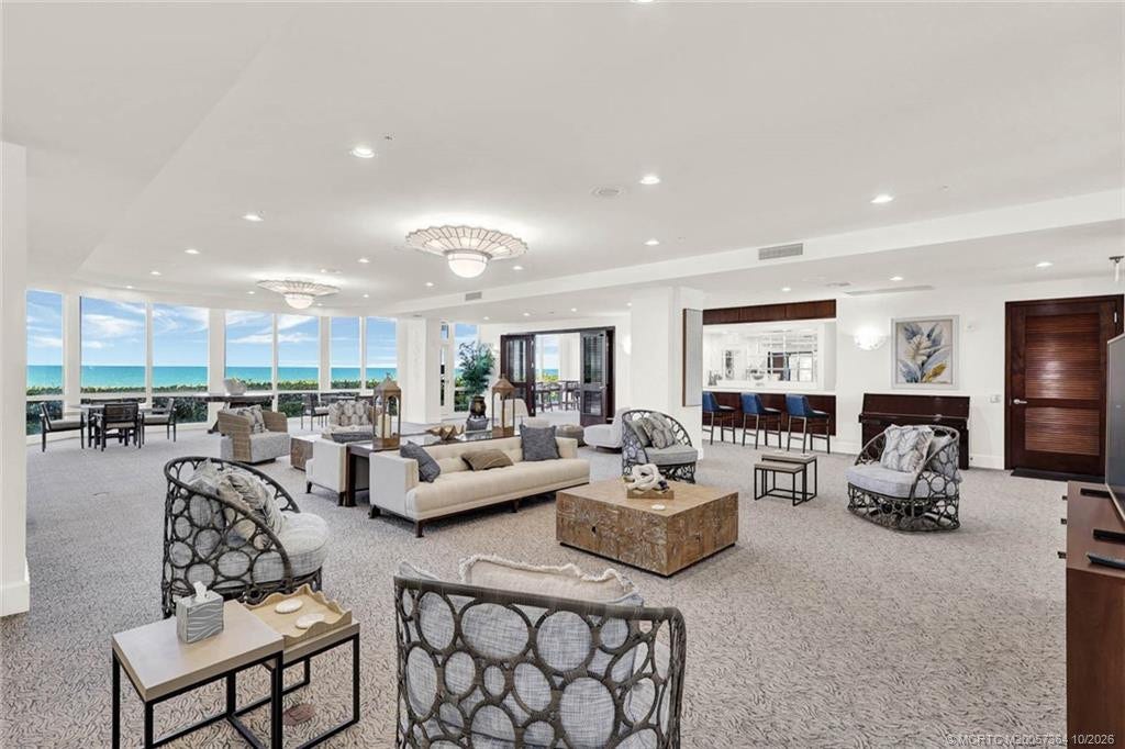 Beautifully furnished community social room featuring spacious seating areas, coastal dcor, and expansive windows overlooking the Atlantic Ocean.