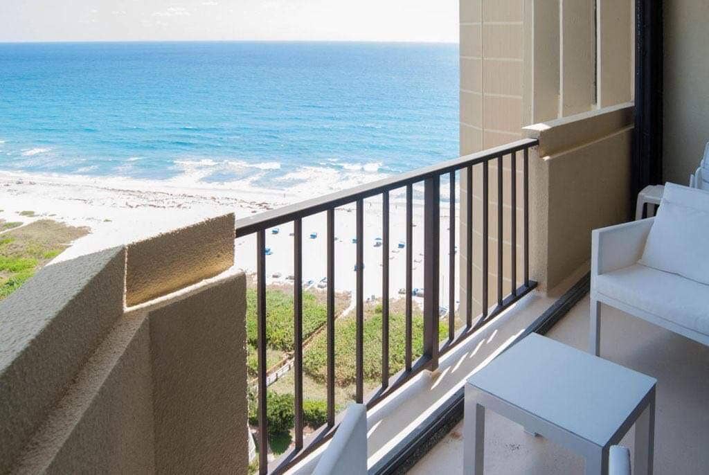 Balcony with metal railings, a stone-textured exterior wall, and coastal scenery