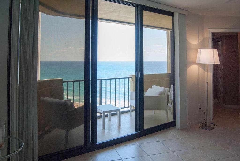 Expansive oceanfront balcony with black metal railing, accessible via multi-panel sliding glass doors