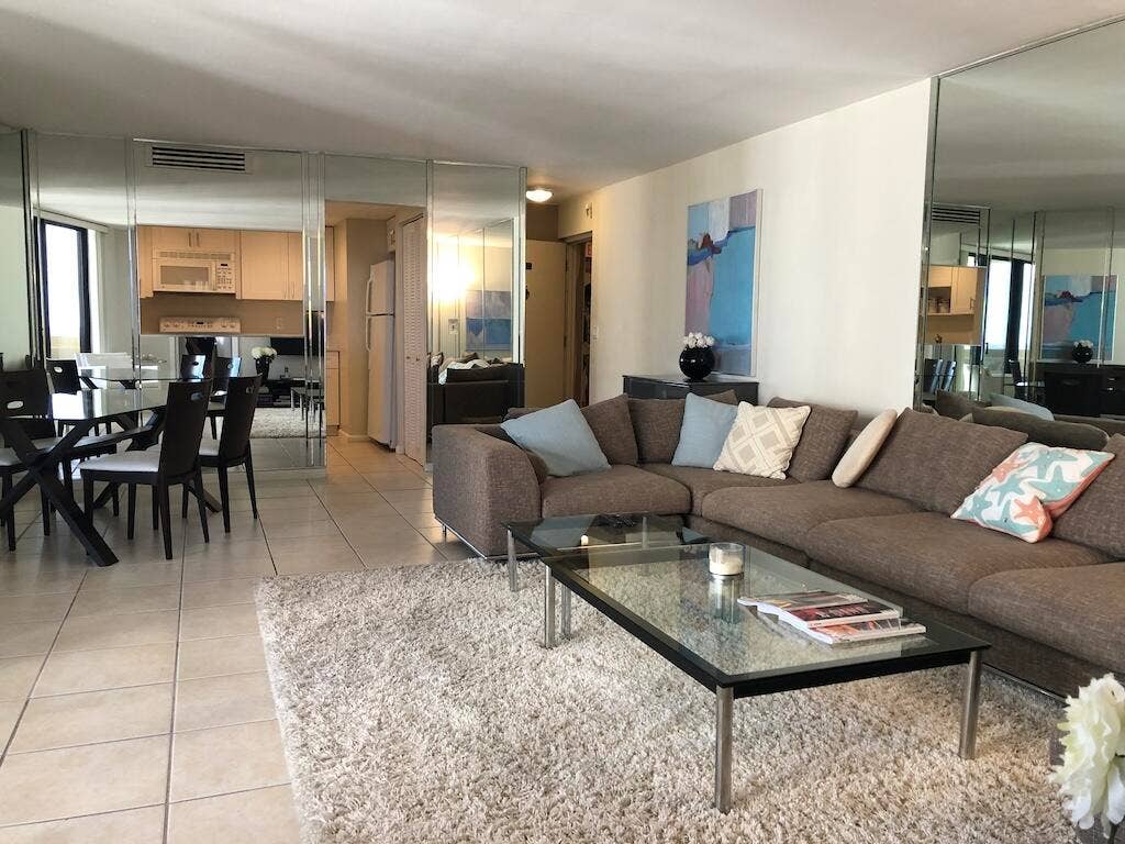 Open-concept living space with tile flooring, mirrored accent walls, and a recessed kitchen